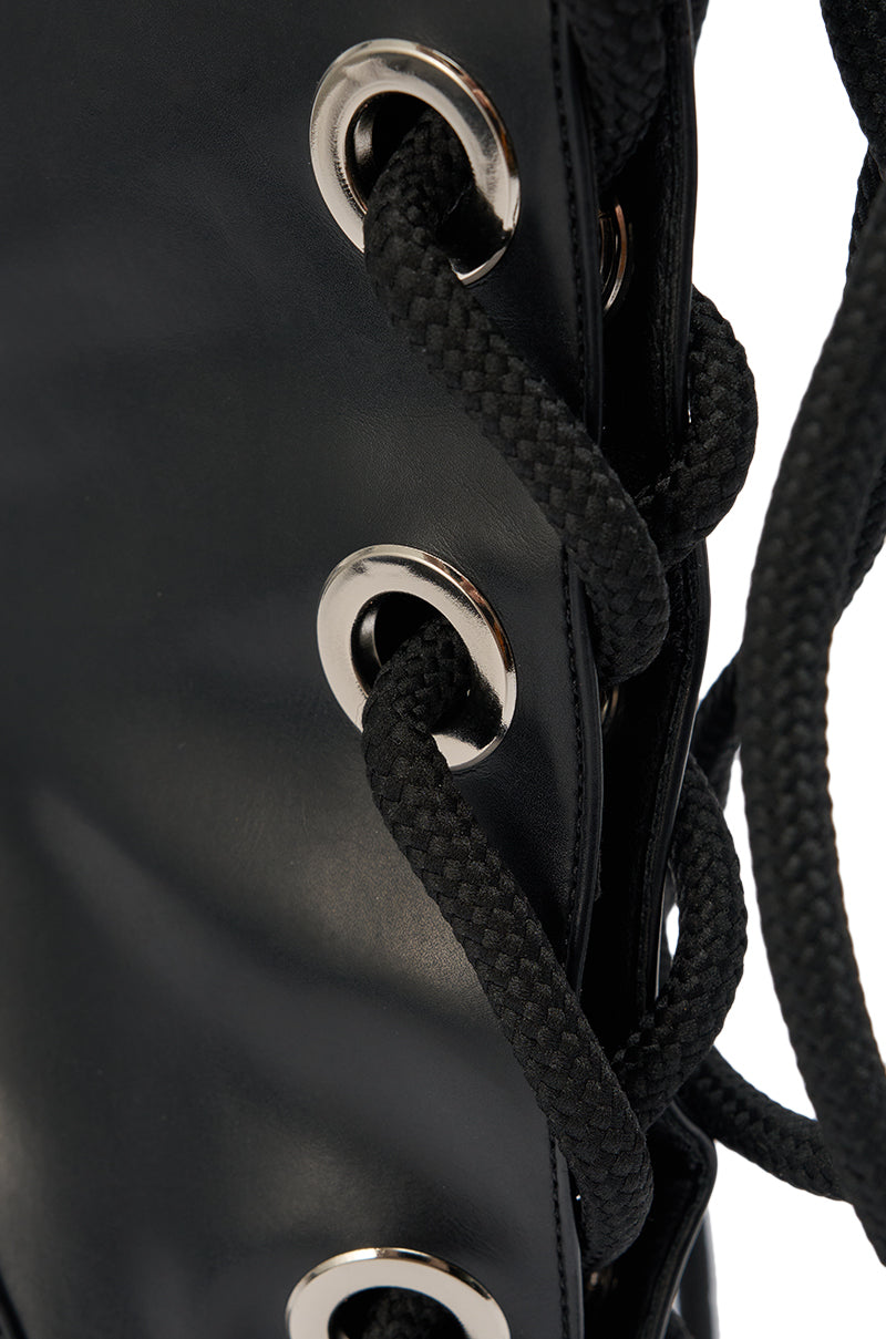 Close-up of black laces threaded through silver eyelets on a smooth black surface, part of the AKIRA GOLD PANTOUM BLACK PU HARDWARE BOOT in sleek faux leather. 8