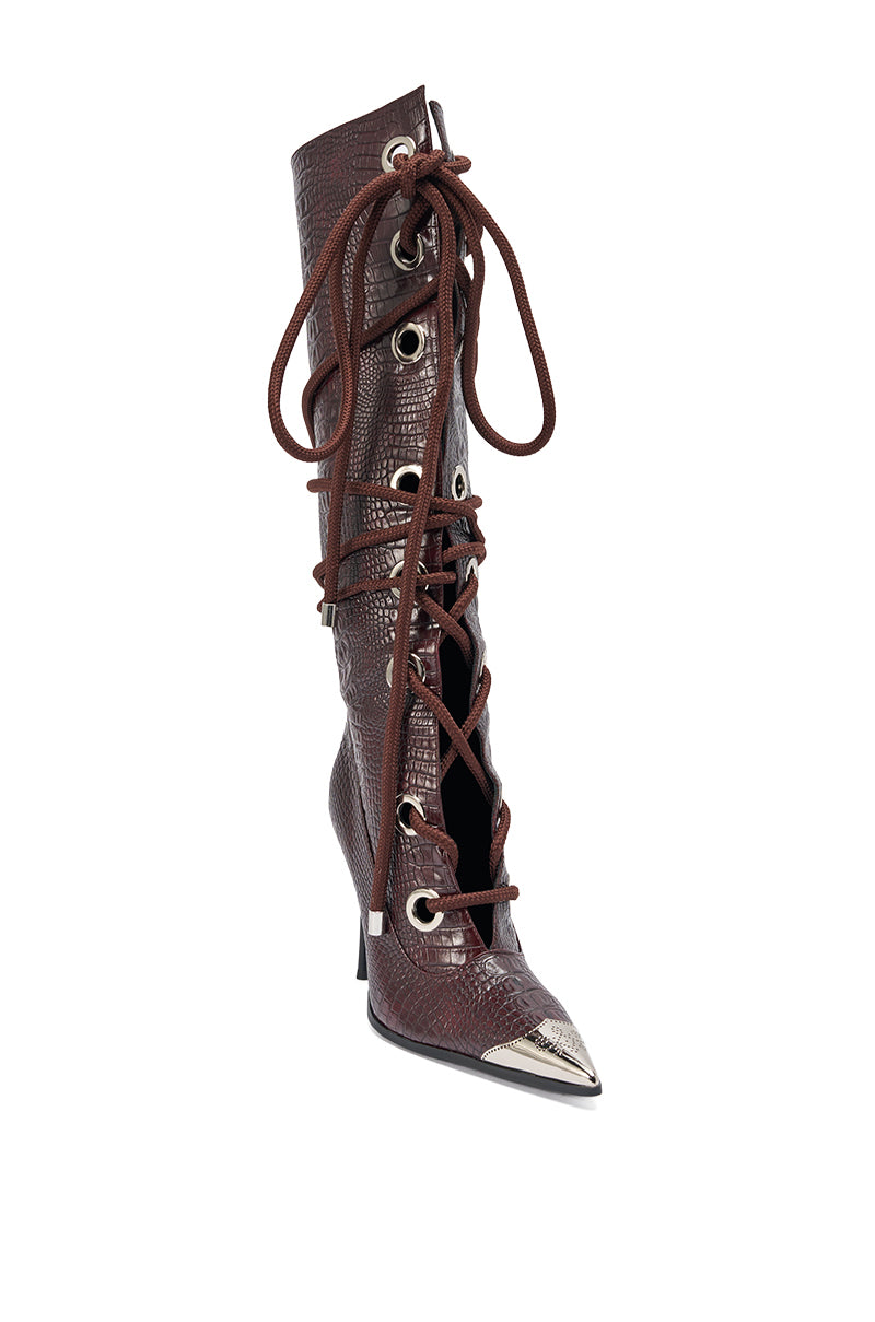 The AKIRA GOLD PANTOUM CHOCOLATE CROC STILETTO BOOT is a knee-high, brown faux-croc boot with large silver eyelets, dark brown crisscross laces, a pointed metallic-tipped toe, and a mid-height stiletto heel. 4