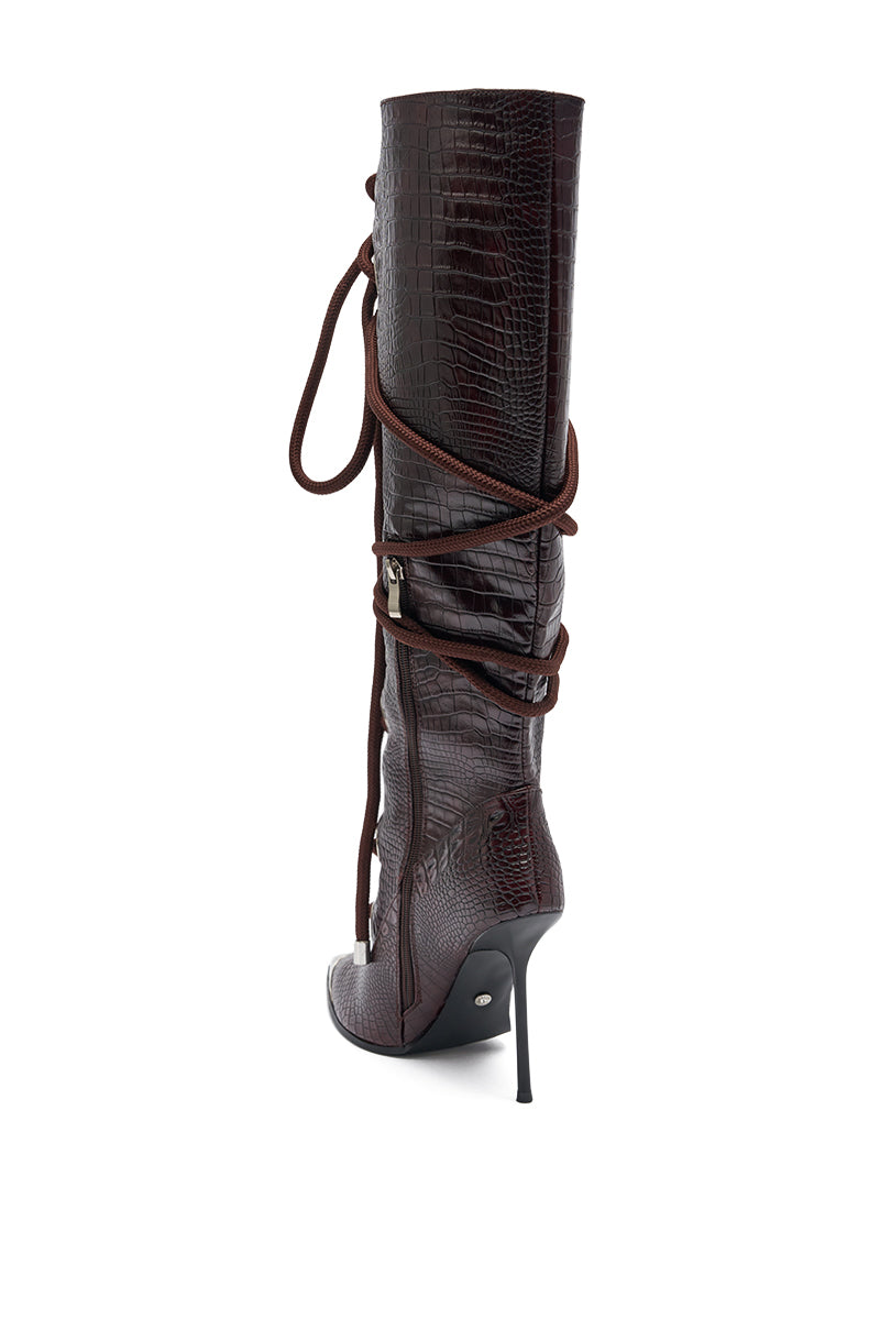 The AKIRA GOLD PANTOUM CHOCOLATE CROC STILETTO BOOT is a tall, dark brown knee-high boot with faux-crocodile texture, pointed toe, side zipper, and long lace wrapping the shaft, shown against a white background. 5