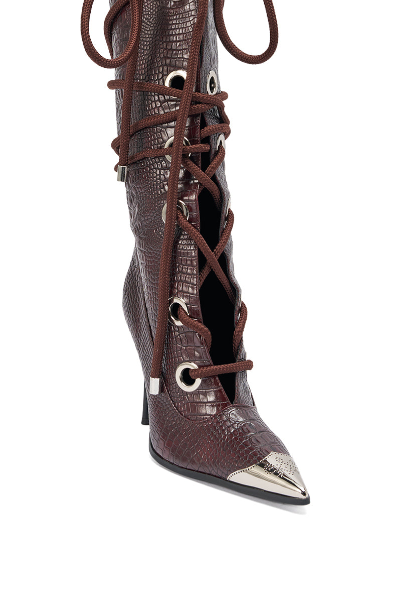 The AKIRA GOLD PANTOUM CHOCOLATE CROC STILETTO BOOT is a brown, knee-high lace-up boot featuring a pointed toe, faux-crocodile texture, large metal eyelets, long brown laces, and a metallic toe cap. 6