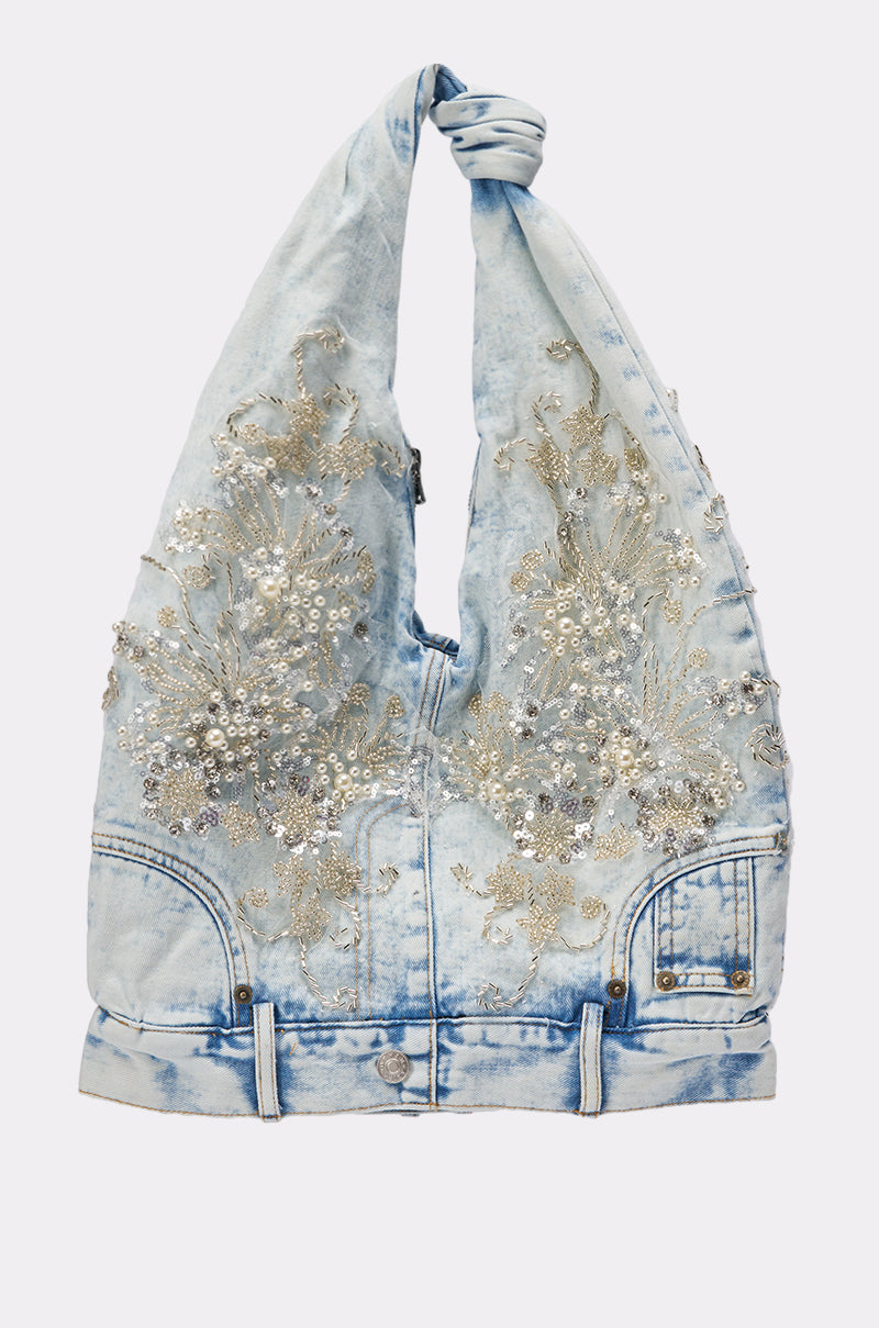 The BLESSING IN DENIM EMBELLISHED SHOULDER BAG features light blue acid-wash denim, a knotted handle, silver floral sequin embroidery, and jacket-inspired pockets and buttons by AKIRA Label. 0