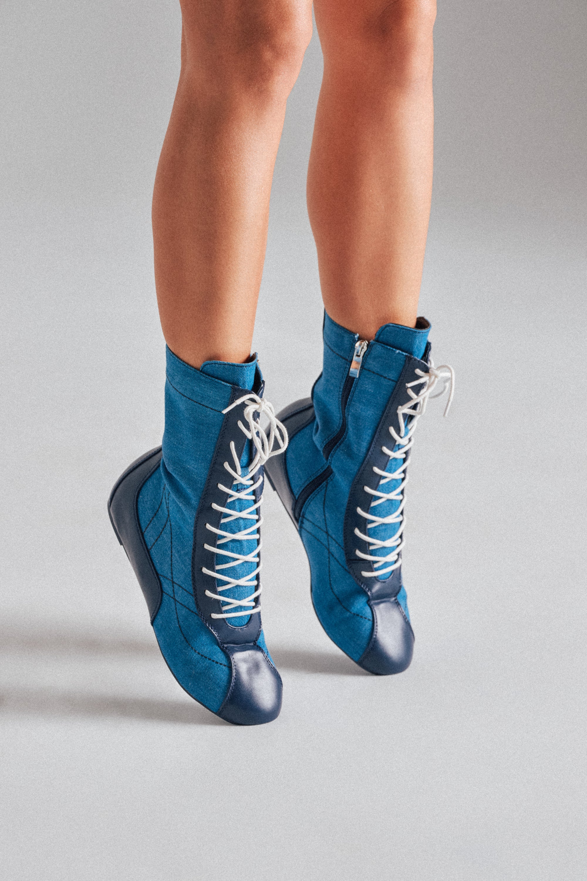 A pair of legs wearing AZALEA WANG PASSER NAVY FLAT SNEAKERS with white laces and rounded toes, standing on tiptoe against a plain light gray background.