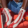 A person wearing the AZALEA WANG PASSER SPORTY FLAT BOOTIE, denim shorts, and a colorful beaded bracelet sits on a bright red bench, with focus on their legs and boots.