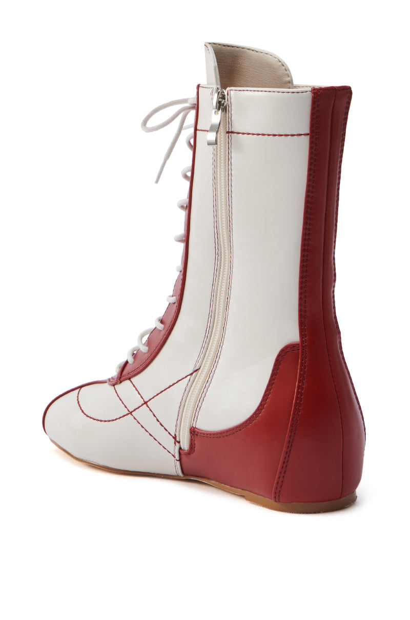 The AZALEA WANG PASSER SPORTY FLAT BOOTIE features a sleek white faux leather body with red accents, a lace-up vamp, side zipper, and red stitching. It stands on a flat brown sole, combining style and functionality.