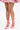 A woman stands against a white background in a pink tweed skirt and the AZALEA WANG PAVARTI PINK BALLET PUMP, featuring ribbon ankle ties, a square toe, and an inverted wedge heel, crossing her feet to show off the modern design.