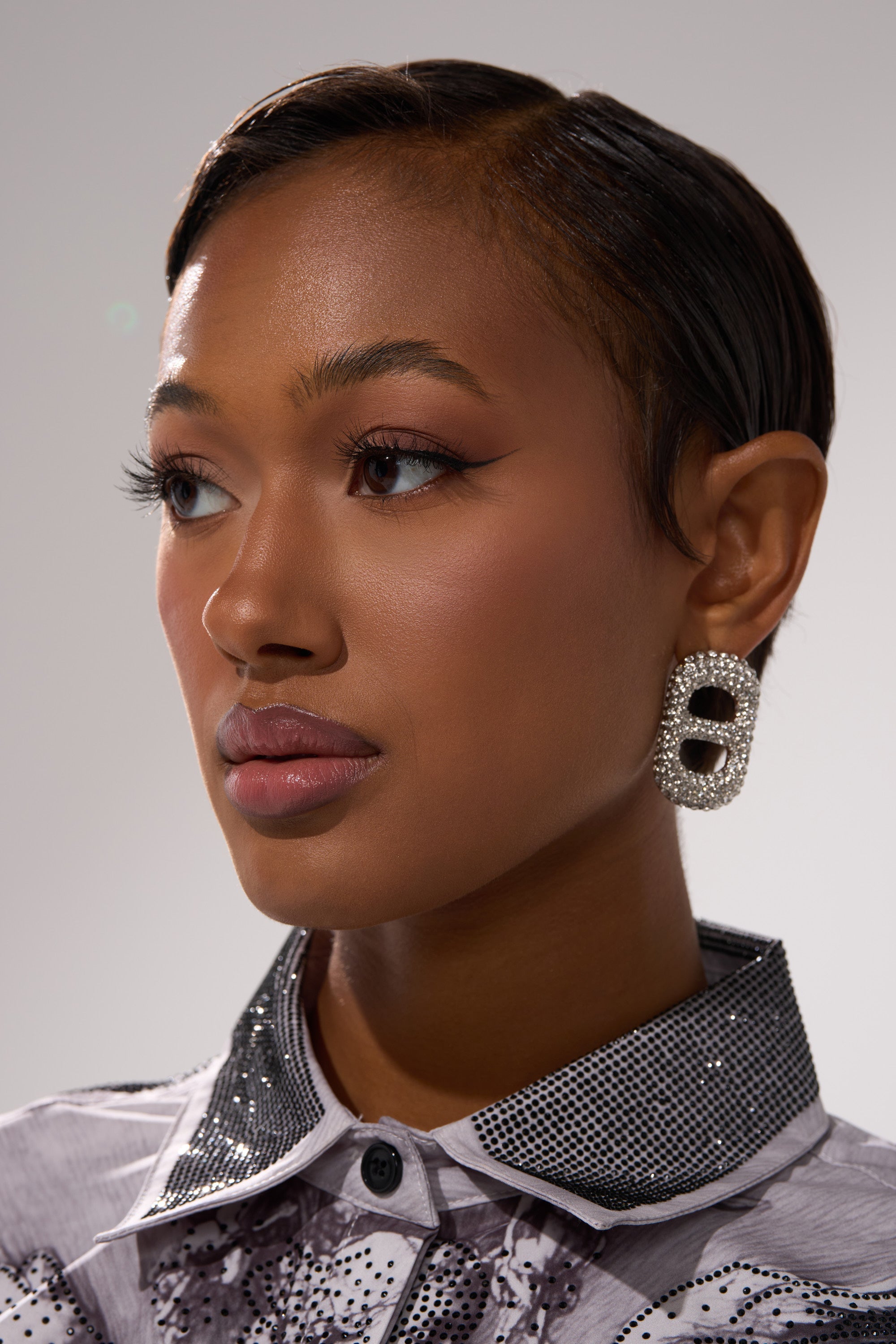 A woman with short, sleek hair wears the POP IT EARRING—sparkling rhinestones catching the light—paired with a collared shirt featuring sequins and metallic accents, gazing to the side against a plain background. 1