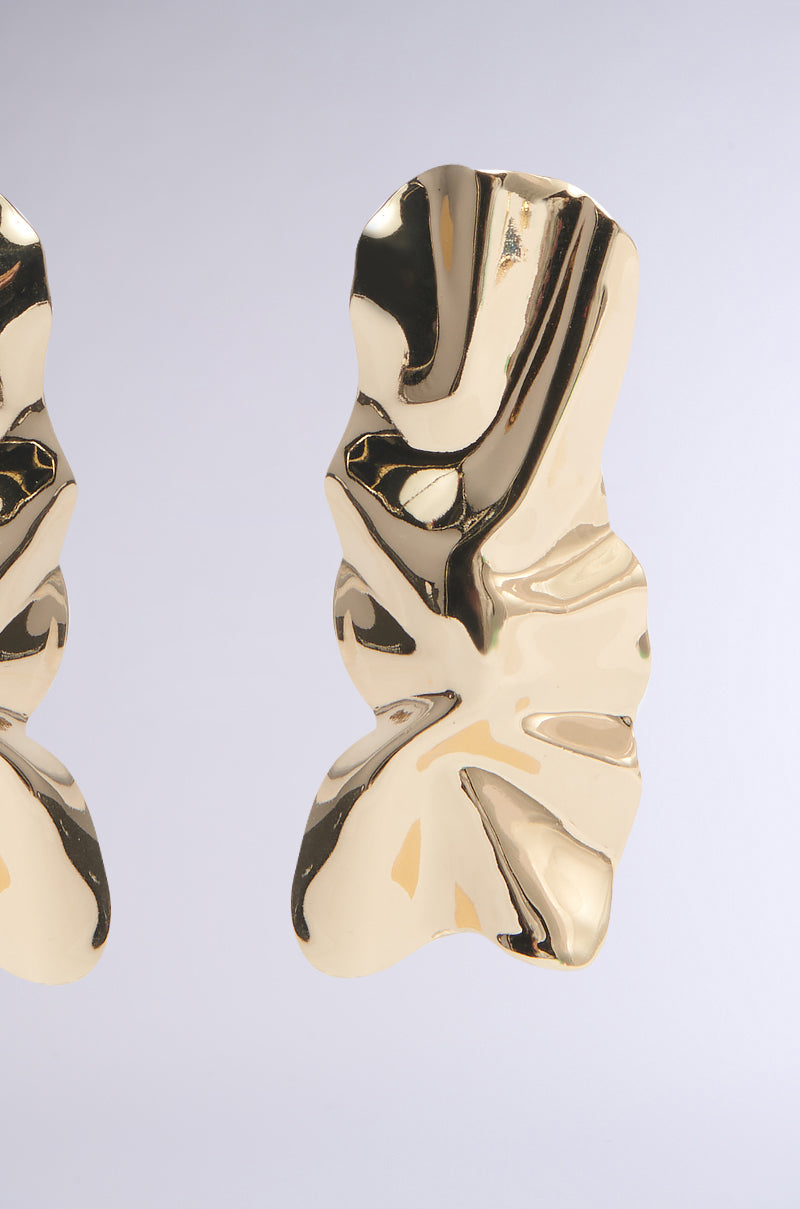 The ITS ORGANIC EARRING features two abstract faux gold earrings with a wavy design on a light gray background. Their textured surfaces are shiny and reflective, highlighting smooth, irregular contours that captivate the eye. 3