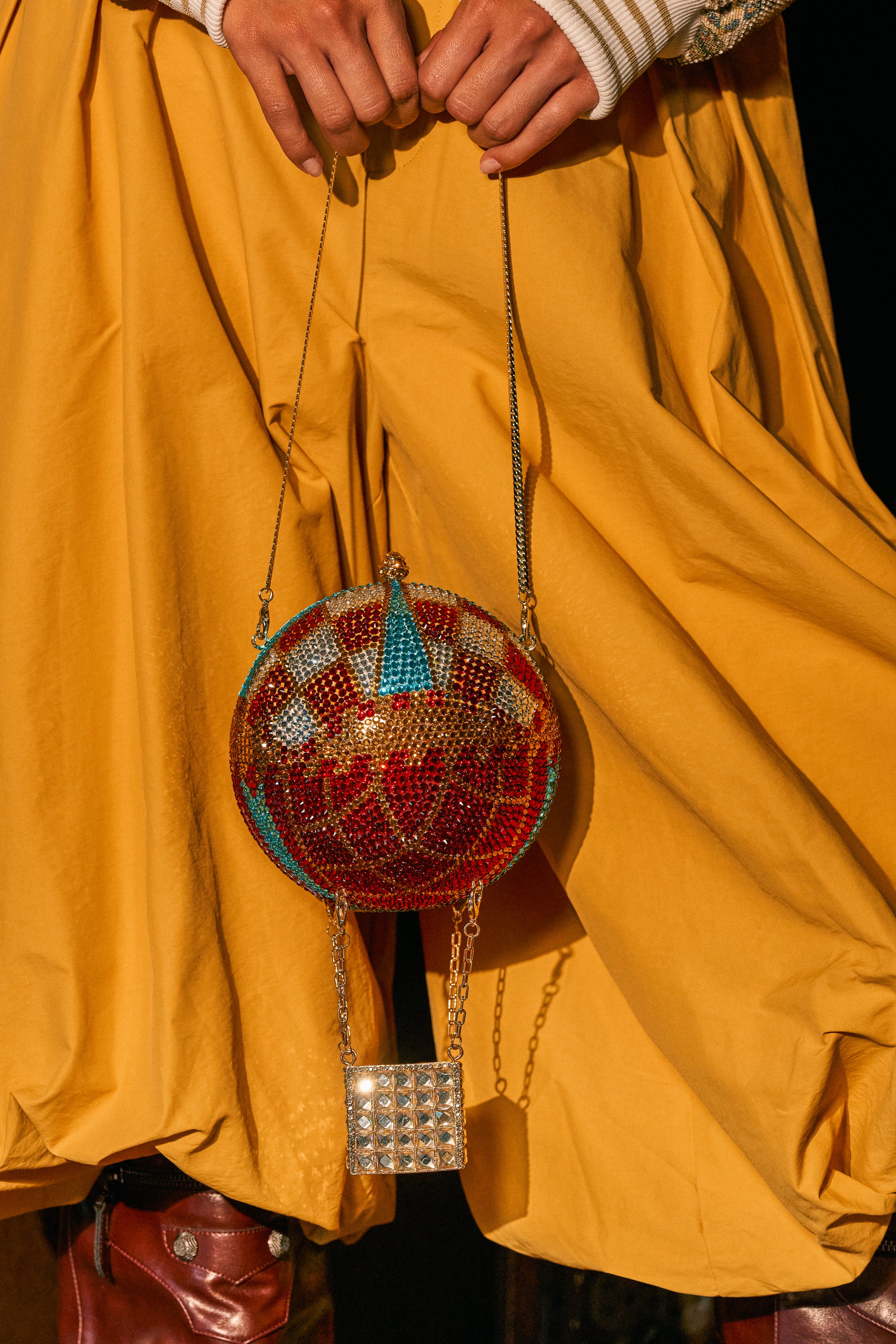 A person in yellow pants holds the CHECK THE VIEWS BLING PURSE, a novelty statement bag shaped like a rhinestone hot air balloon with beaded details, a chain handle, and a small square basket.