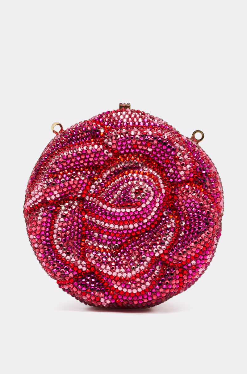 The NOT THAT KIND OF ROSE PURSE is a novelty hardshell handbag adorned with pink, red, and magenta rhinestones in a rose design, featuring small gold loops at the top for strap attachment.