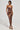 A woman poses in the HEAVEN SENT MESH MIDI DRESS, a form-fitting, strapless piece adorned with sequins and abstract patterns in earthy tones. The dress's ruched construction accentuates her silhouette as she stands elegantly in strappy high-heeled sandals against a plain, light-colored background.