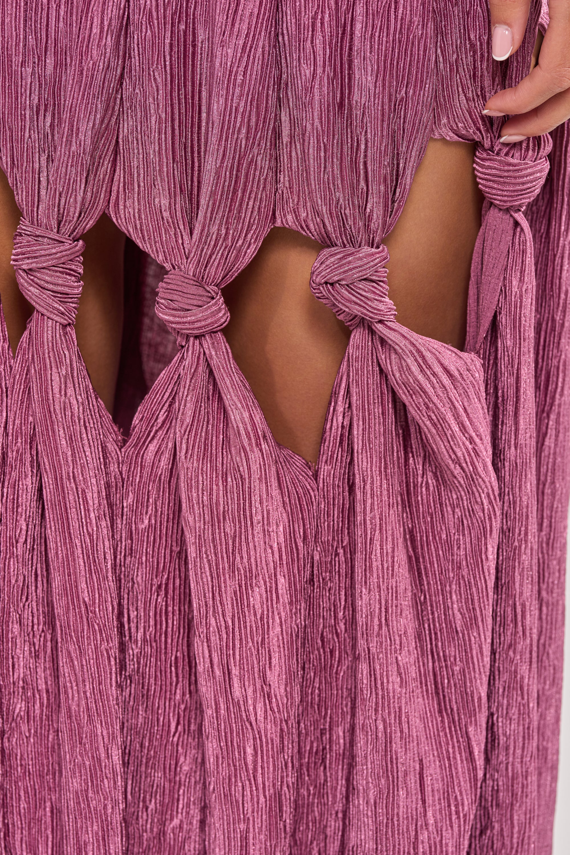 Close-up of the BORN READY KNOTTED STRAPLESS MAXI DRESS in mauve satin, featuring a crinkled texture, knot detail, and diamond-shaped cutouts. A hand rests on the skirt—an ideal chic choice for wedding guests. 4
