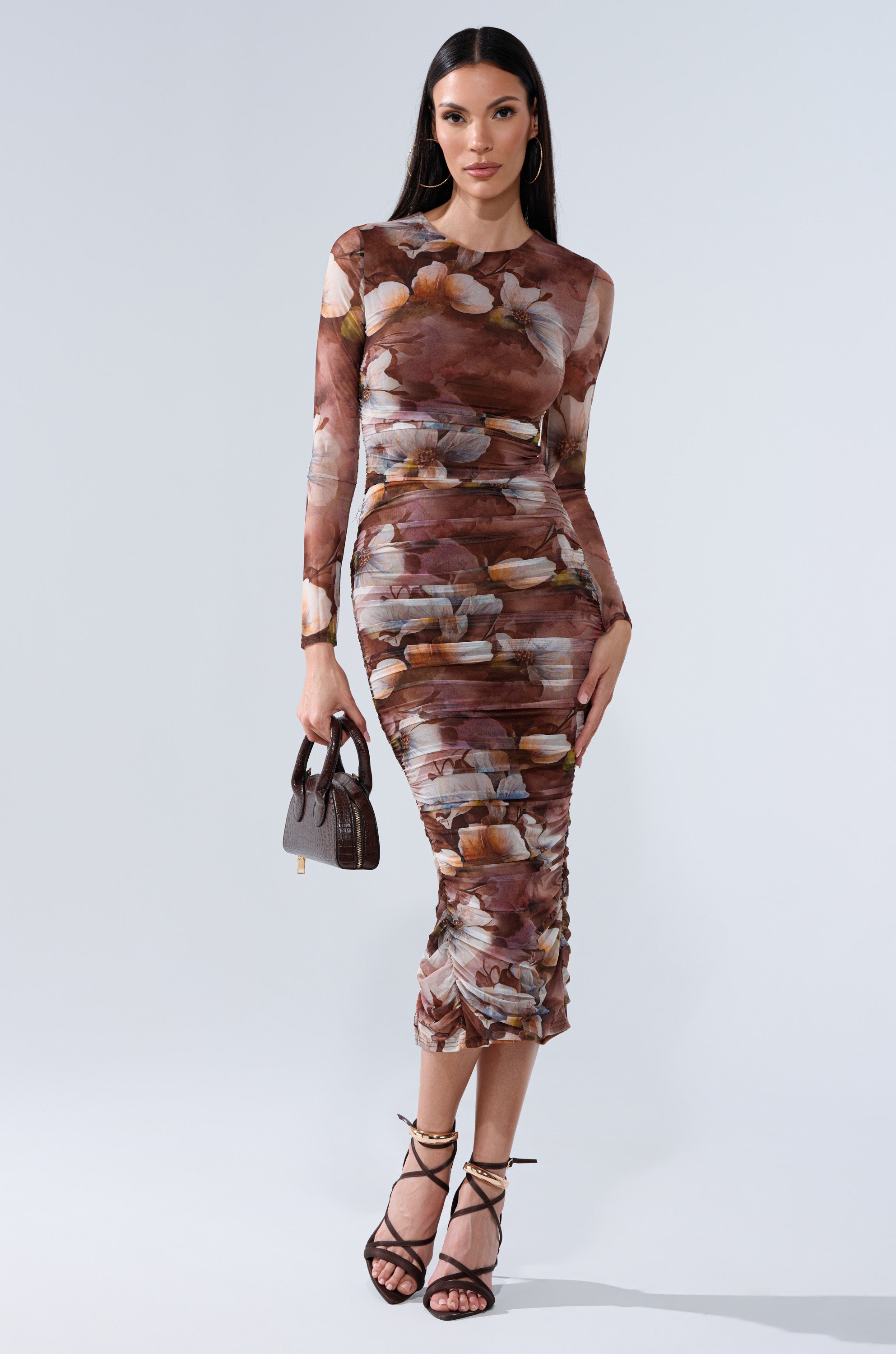 A woman models the FELT CUTE PRINTED MIDI DRESS, a fitted floral midi dress, paired with a small brown handbag and strappy black heels against a plain light backdrop. 1