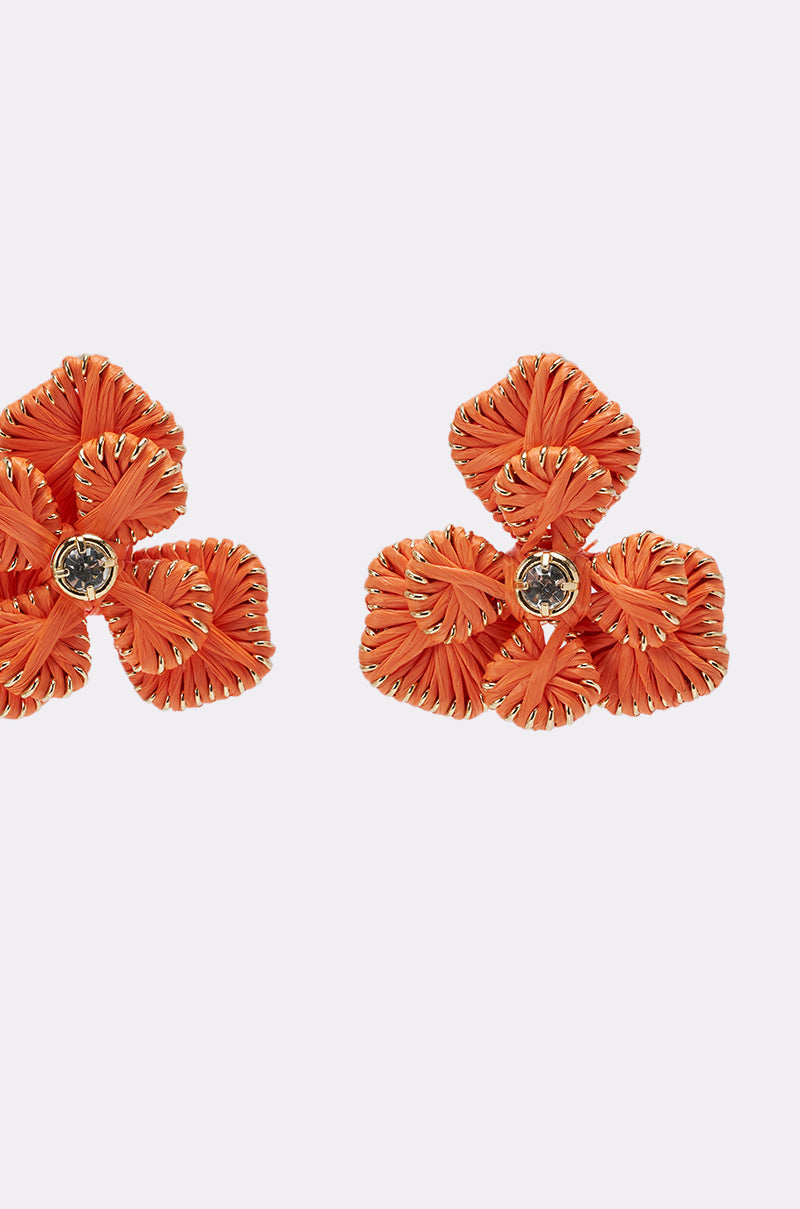 The ON THE BEACH EARRINGS feature two orange floral statement pieces with braided petals, gold accents, and central gemstones, displayed against a plain white background. 3