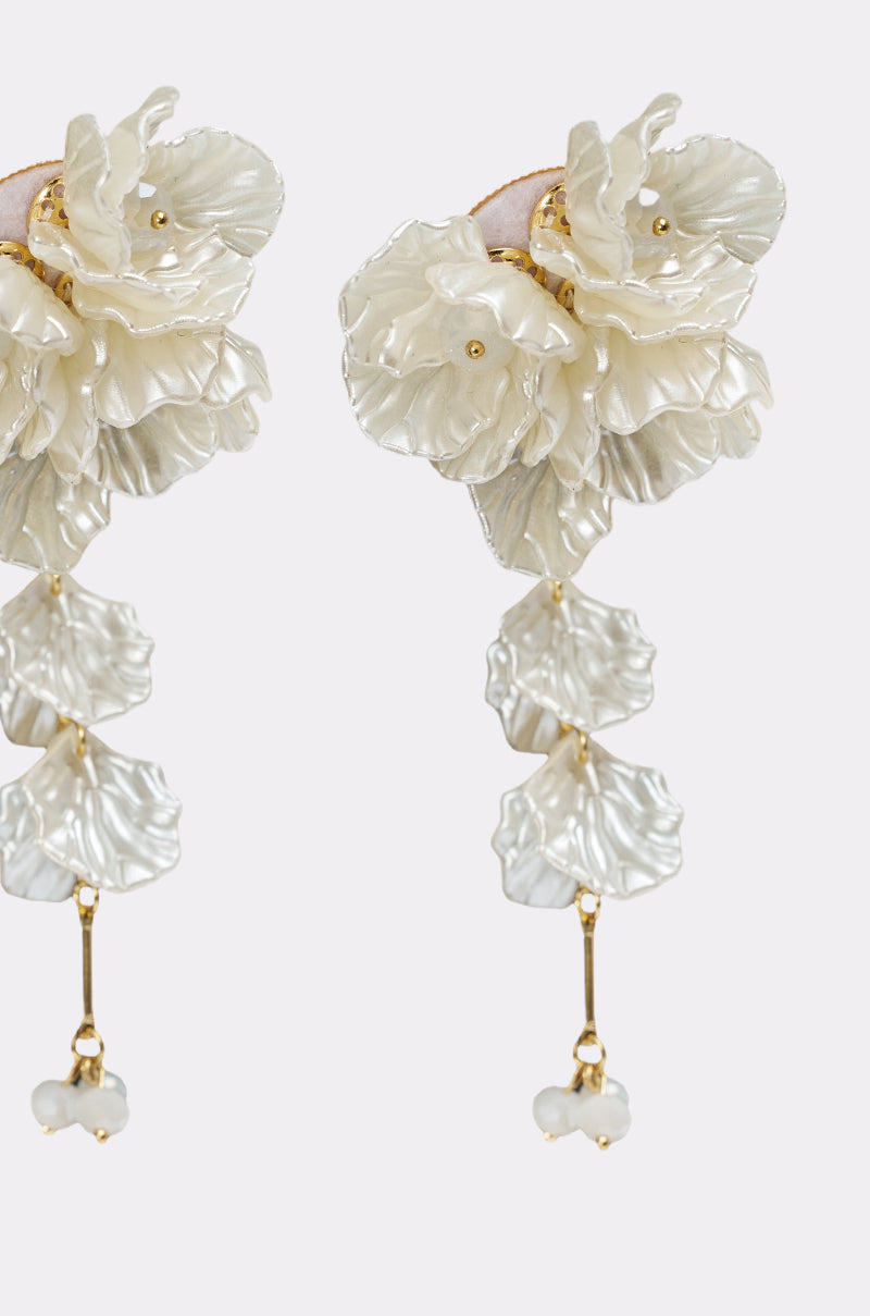 Close-up of FOR THE PARTY EARRING—ornate floral petal earrings with layered white elements, gold accents, and cascading drop design ending in small white beads—set against a plain light background. 3