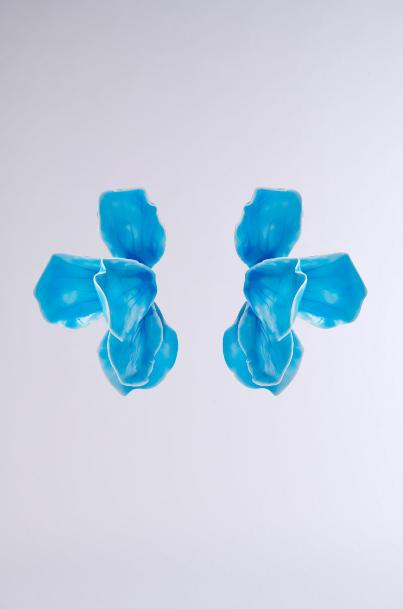 Two symmetrical, abstract blue shapes with fluid, petal-like forms appear against a light gray background, resembling the NO BLUES EARRING from the AKIRA Label collection. 0