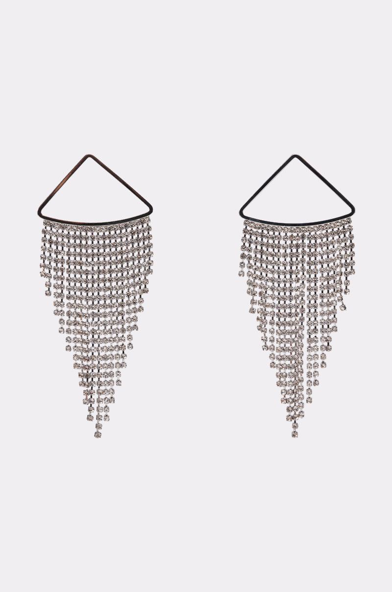 The WE'RE GOING OUT EARRING IN SILVER features geometric chandelier earrings with triangular tops and cascading rhinestone chains that create a shimmering triangular fringe, displayed on a plain light background. 0