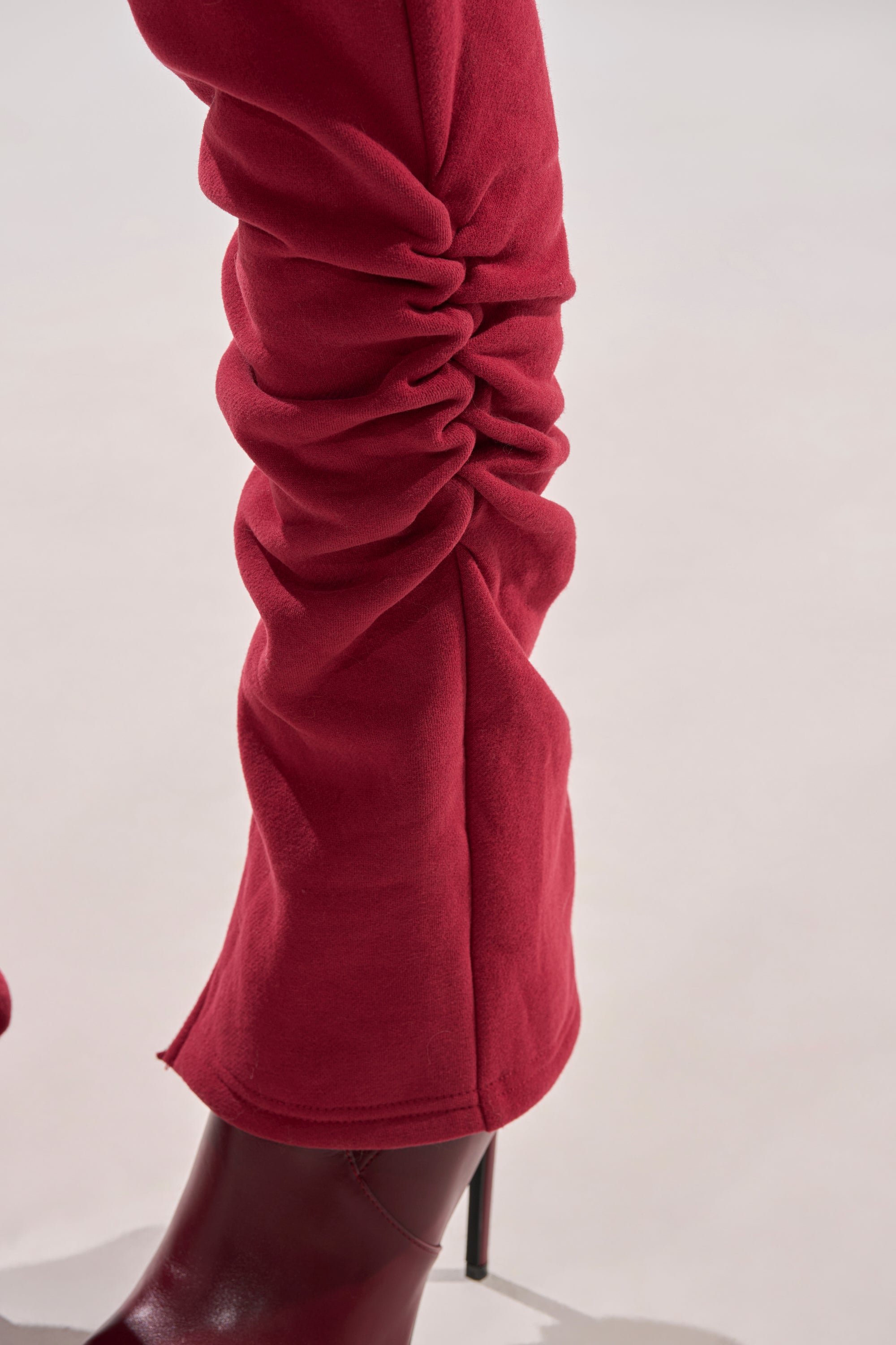 A close-up of a leg in the COZY HOLIDAY PEARL JOGGER IN BURGUNDY, featuring pearl embellishments, paired with a matching red pointed-toe heeled boot against a plain light background.