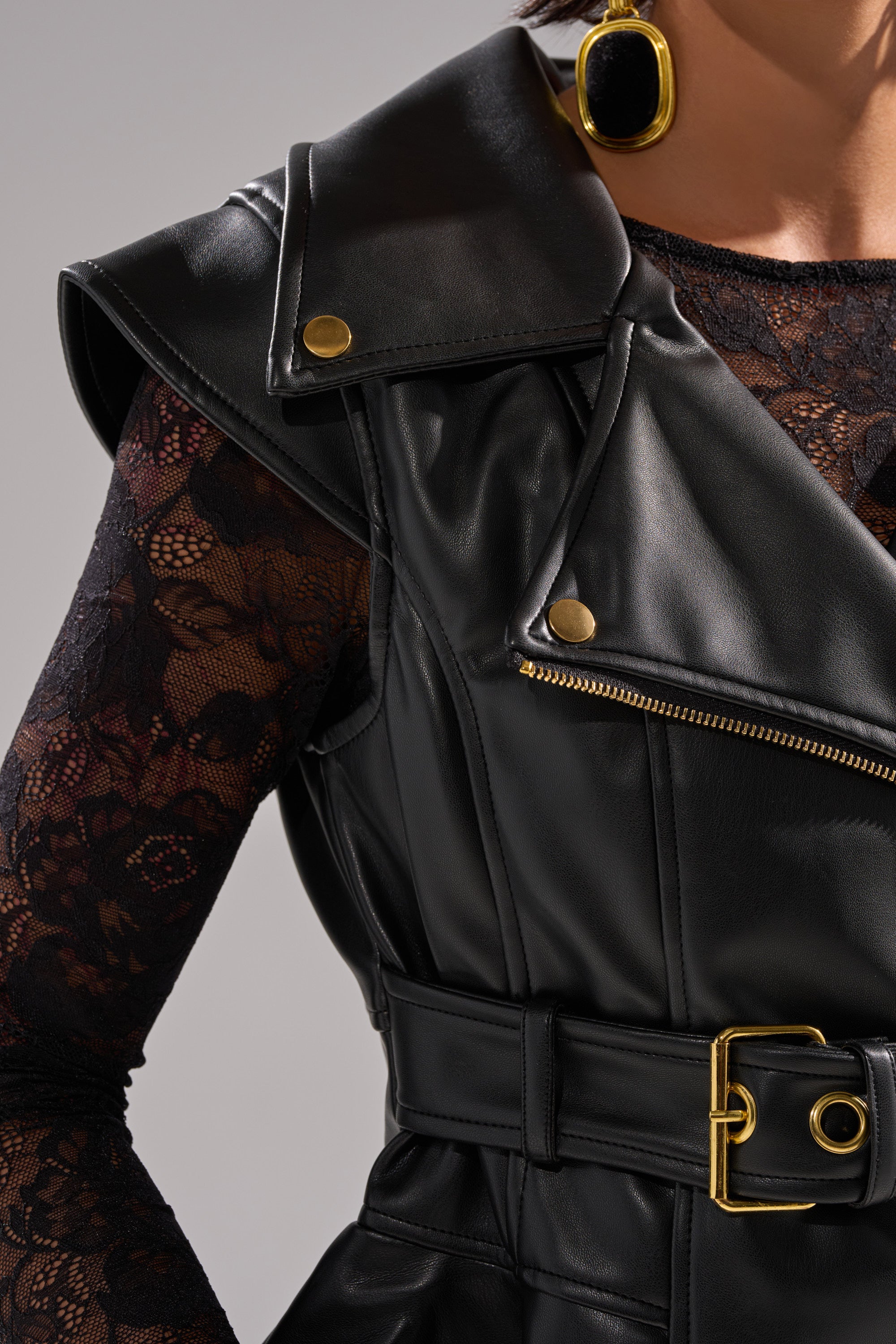 A close-up of a person wearing the PEP IN MY STEP LEATHER VEST styled with a black lace long-sleeve top, a wide adjustable waist-belt, and bold black and gold earrings. 11