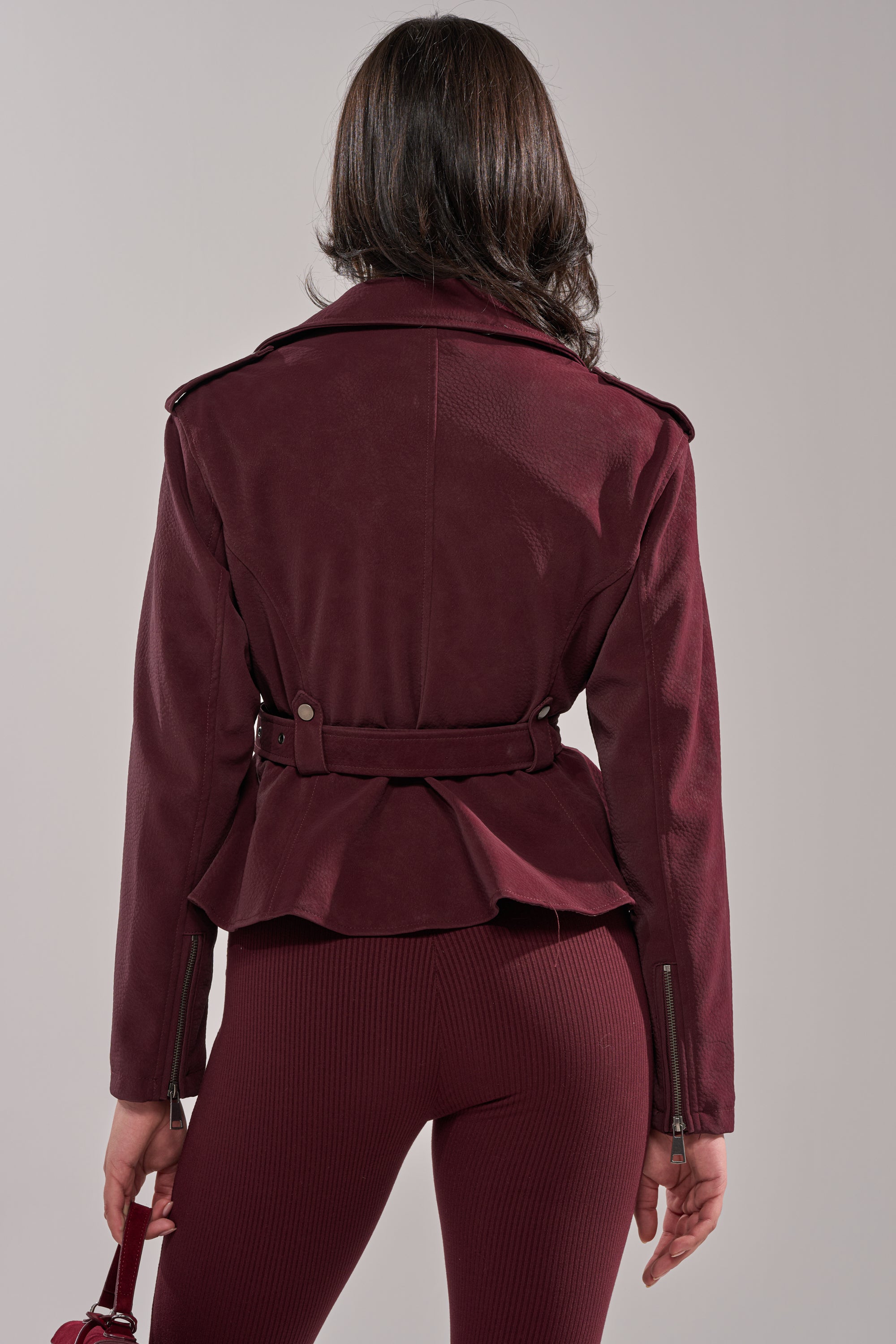 A woman models the DANI SUEDE EFFECT PEPLUM MOTO jacket with shoulder epaulets and matching ribbed pants, showcasing a tailored feminine silhouette from the back against a neutral background. 4