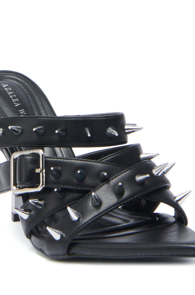 A close-up of the AZALEA WANG PEREGRINE BLACK STUD AND SPIKE MULE SANDAL, featuring silver spikes, a square buckle, faux leather construction, multiple straps, a low block heel, and visible branding on the insole. 6