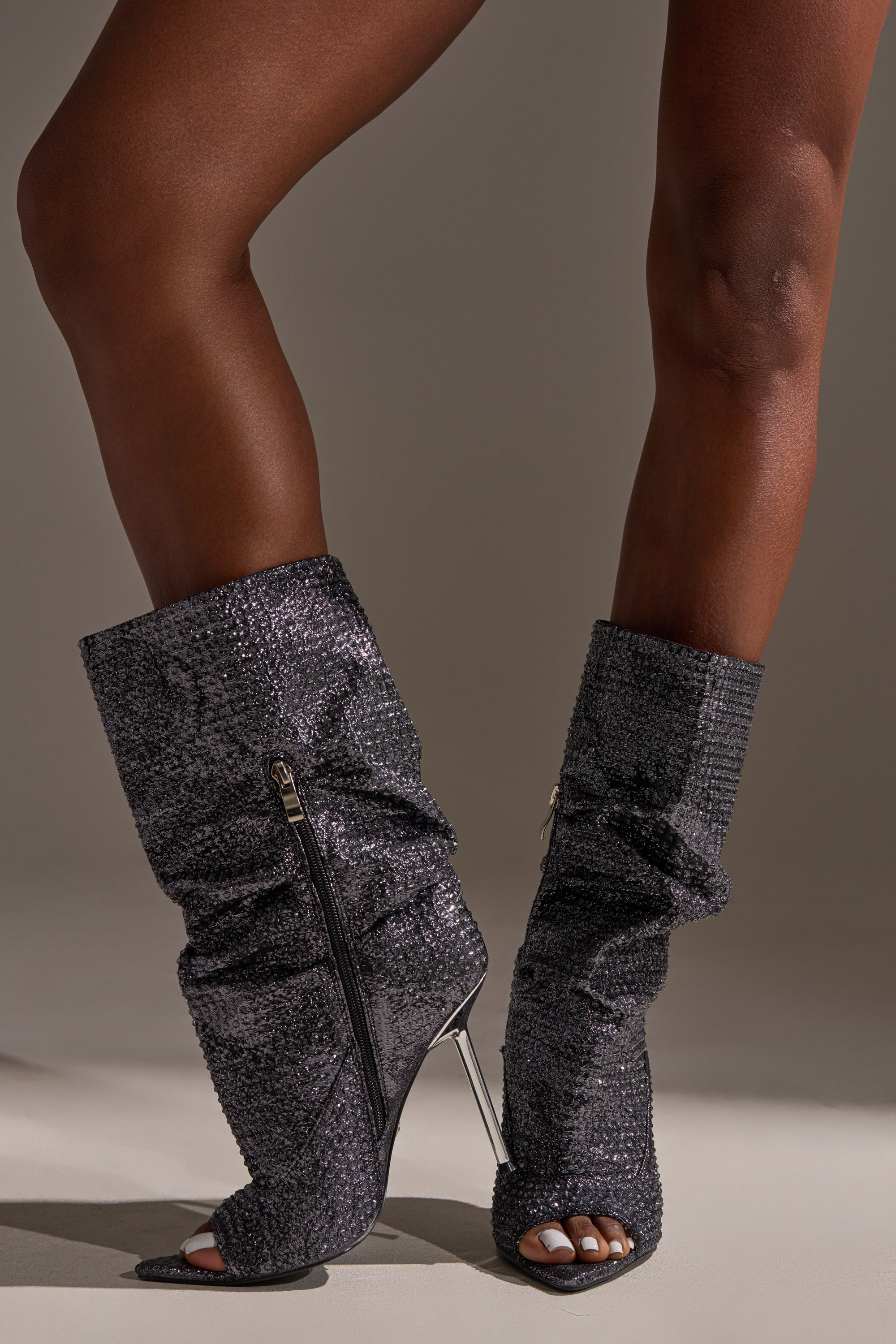 A close-up of legs wearing the AZALEA WANG PHOTINE BLACK MULTI SPARKLE OPEN TOE STILETTO BOOTIE, featuring sparkling rhinestones, a knee-high slouched textured look, open toe design, side zippers, and added glamour.