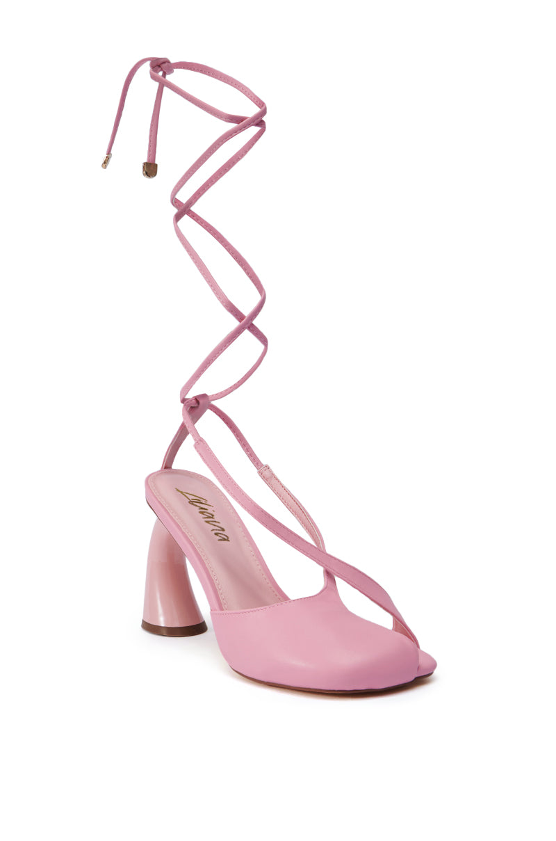Introducing the PIRATE PINK PUMP: A chic high-heeled sandal in Pirate Pink, featuring crisscross ankle straps that extend elegantly above the ankle and come with a metallic aglet. The closed-toe design is complemented by the brand name "Aquazzura" showcased on the insole. The shoe is finished with a chunky sculpted heel, flawlessly embracing the balletcore trend.