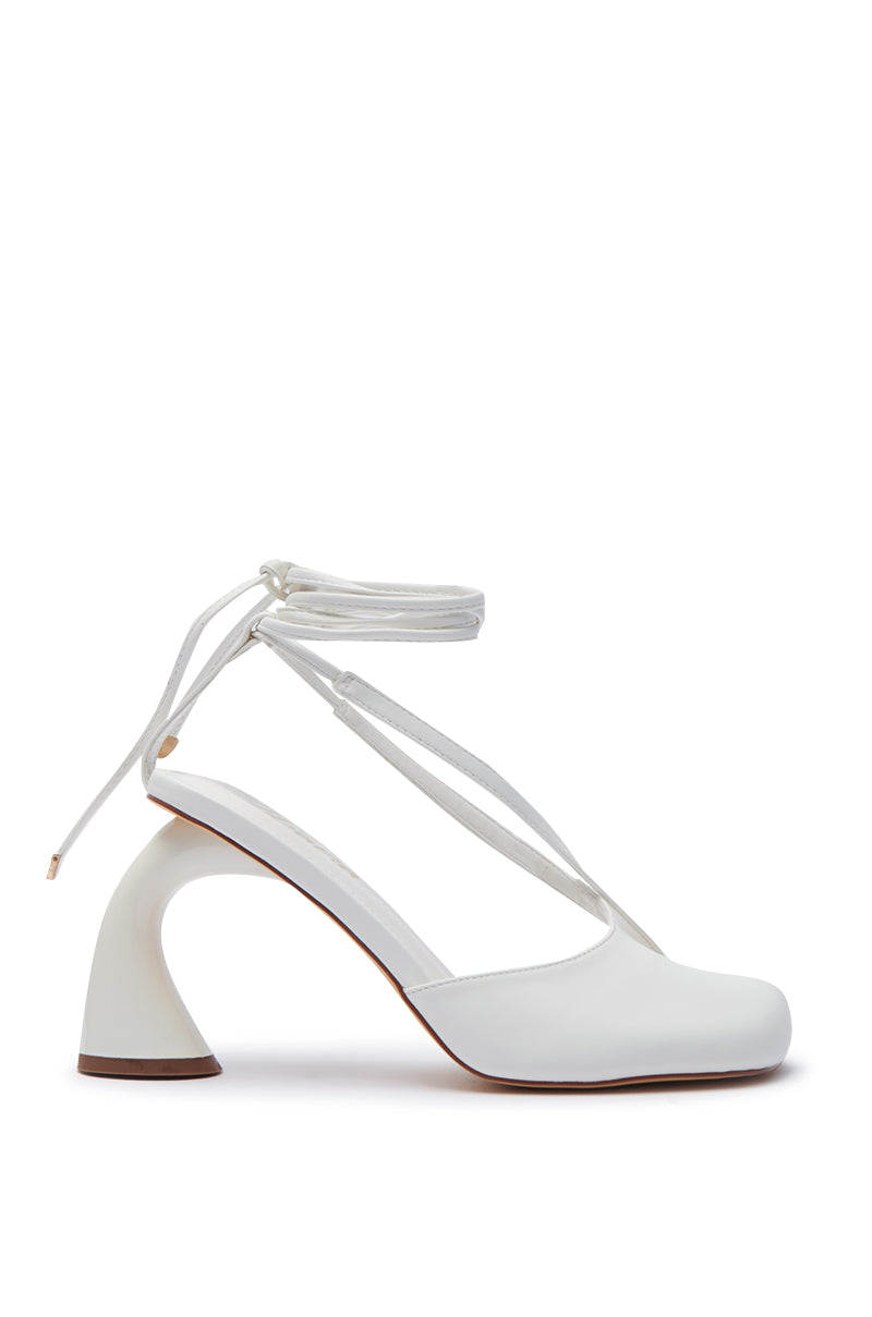 Introducing the PIRATE WHITE PEEP TOE PUMP, a stylish shoe featuring a unique curved heel design and elegant wrap-around ankle straps. Embodying the balletcore trend, this single, white pump is showcased against a minimalist white backdrop.