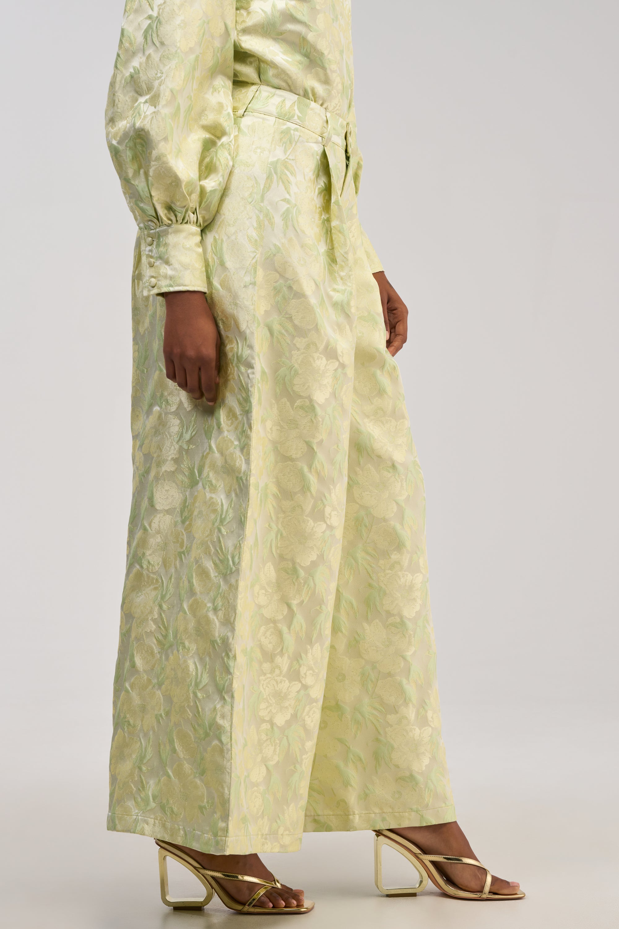 A person is wearing the LOOK THIS WAY SHINY PANT IN GREEN—high-waisted, wide-leg pants styled with a matching top, making them a perfect choice for a stylish holiday party. They’ve paired the look with metallic, strappy heeled sandals against a plain, light-colored background.
