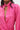 A woman wears the LOOK THIS WAY SHINY BODYSUIT in bright pink, featuring metallic textured fabric, a high collar, rhinestone clasp, and deep V-neckline. Only her torso and lower face are visible.