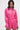 A woman with long dark hair wears the LOOK THIS WAY SHINY BODYSUIT—a bright pink, long sleeve romper with a deep V-neck, choker collar with ring detail, and high-waisted shorts—standing against a plain white backdrop.