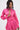 A woman confidently poses against a plain white background in the LOOK THIS WAY SHINY BODYSUIT, a bright pink metallic romper with a matching circular-buckle choker.