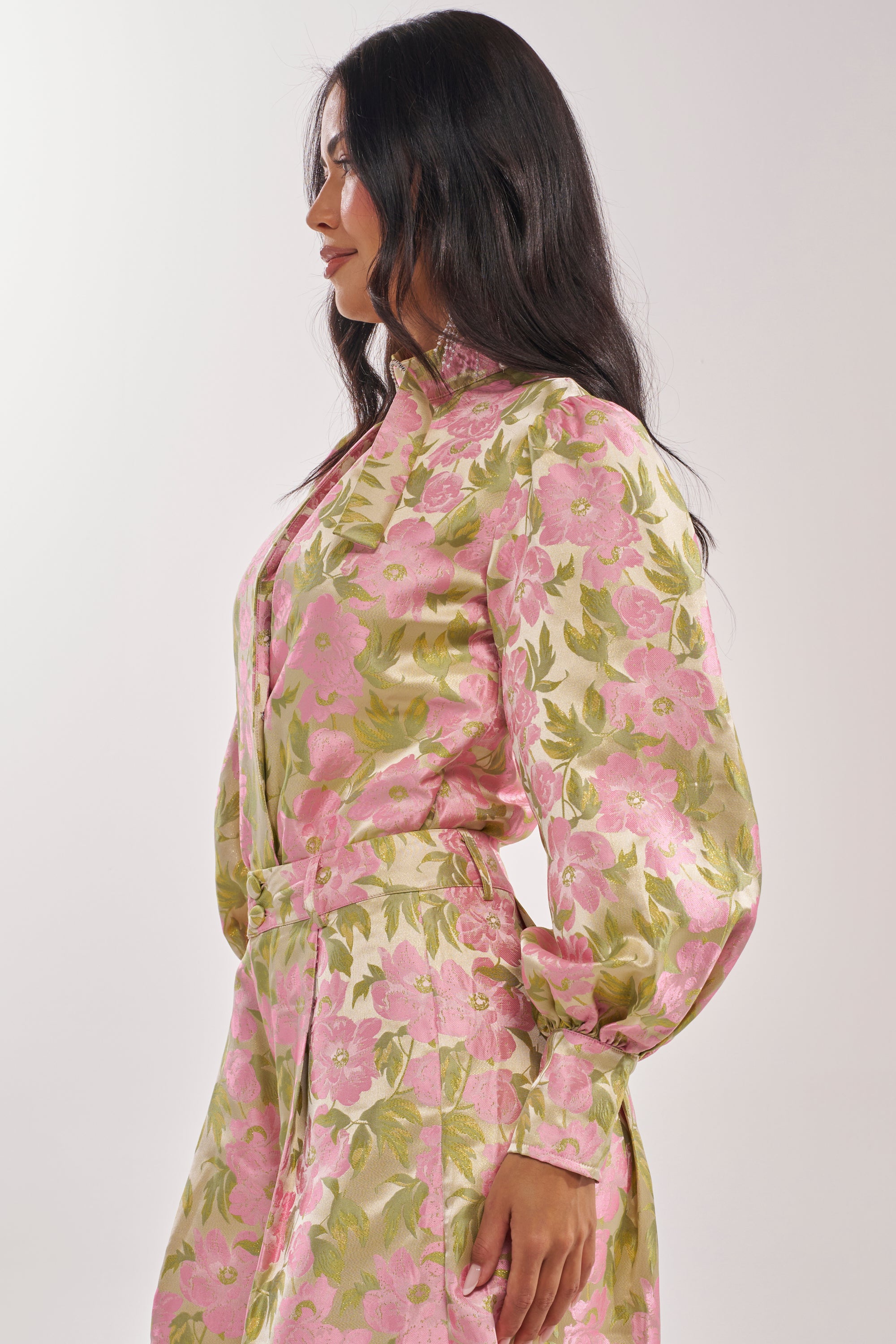 Woman with long dark hair stands in profile against a light background, wearing the OVER IT FLORAL BODYSUIT in pink and green, featuring a romantic shine and floral print. 4