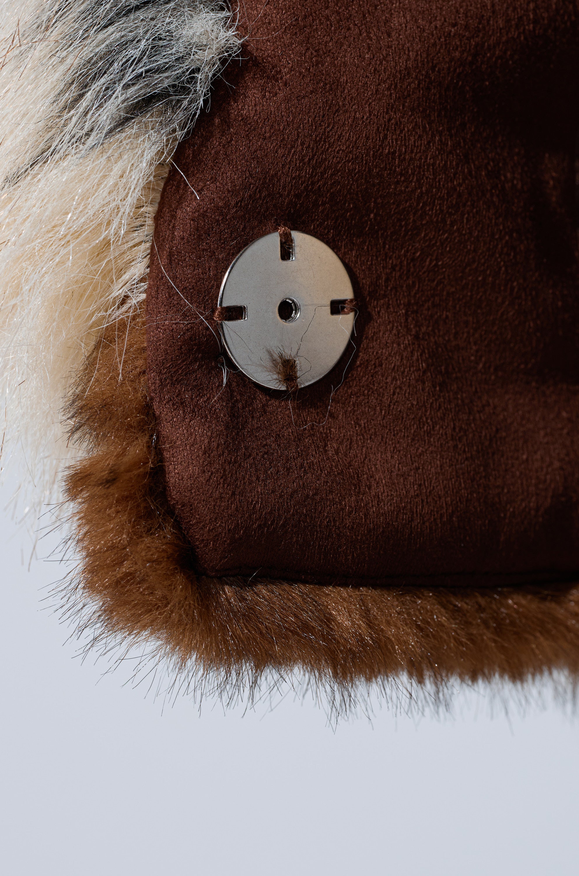 Close-up of the PORTIA CROPPED FAUX FUR JACKET shows plush brown and white faux fur with a shiny silver button—a soft, luxurious texture ideal for women's fashion outerwear.