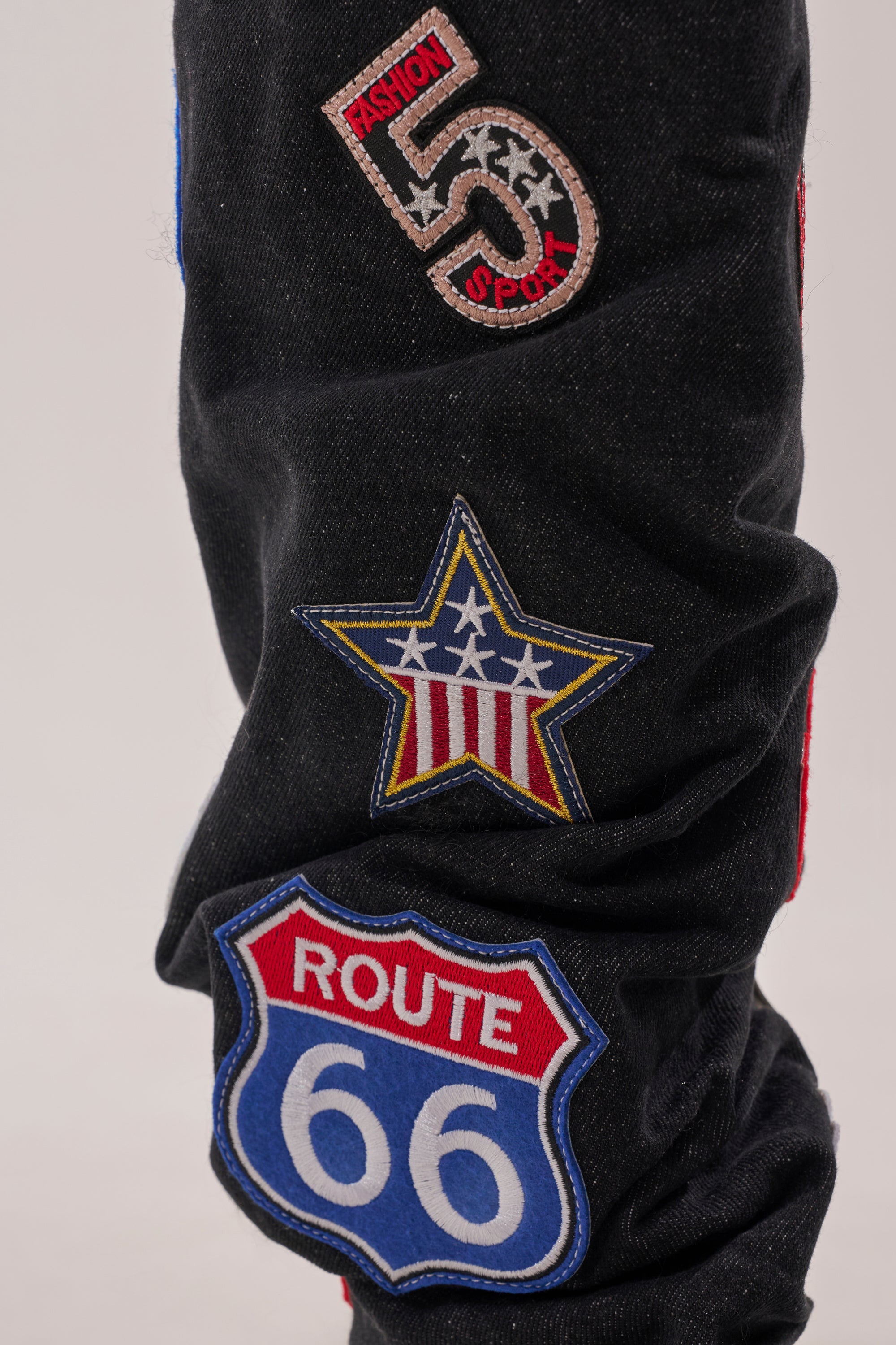 A close-up of black denim jeans with embroidered patches, paired perfectly with the AKIRA GOLD POSTAL BLACK PATCHWORK FLAT BOOT featuring a bold lug sole. 4