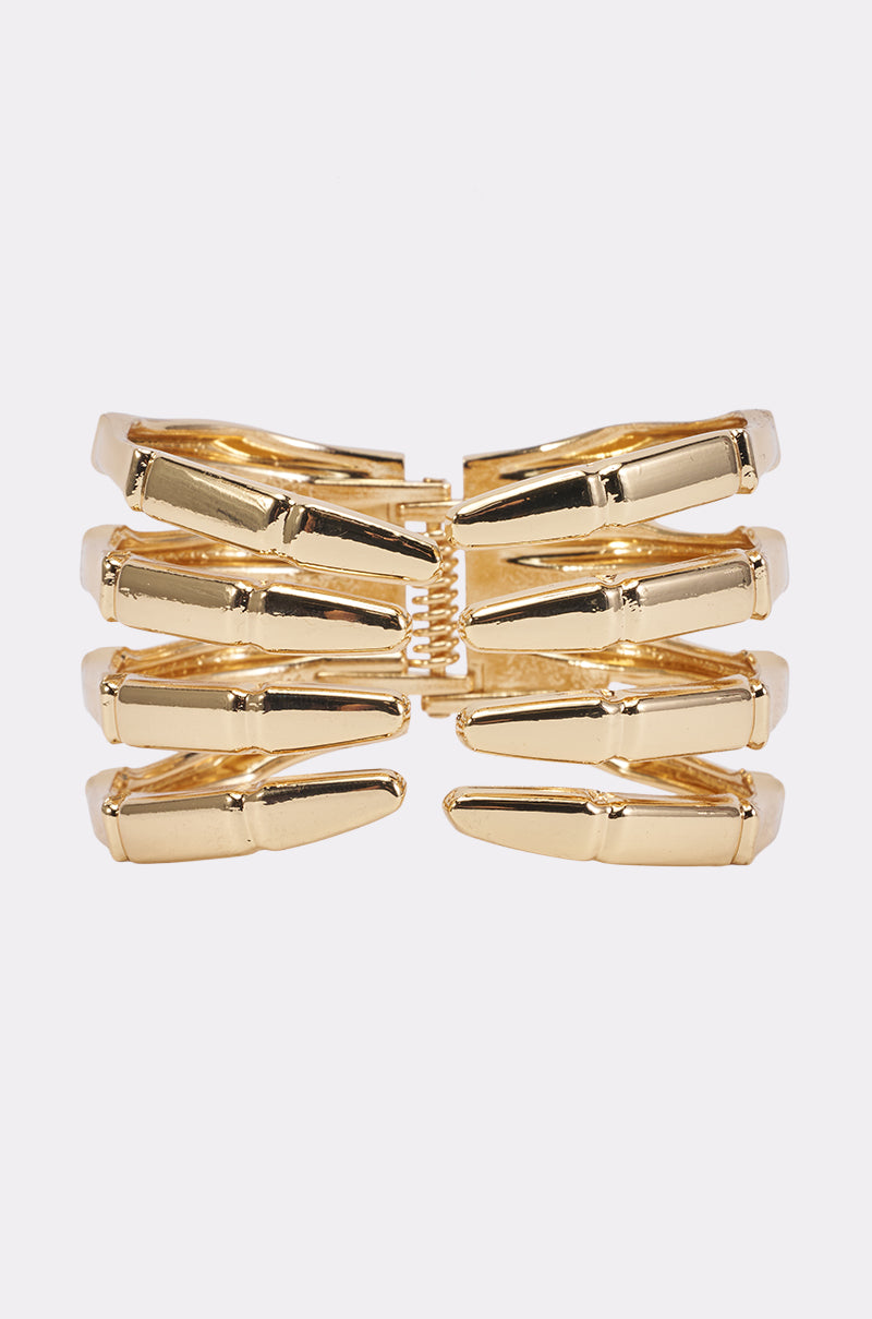 The SKELLY CUFF is a gold hair clip designed in the shape of stylized skeletal fingers, reminiscent of bone-inspired jewelry, and displayed against a plain light background.