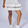 A person dressed in a white tulle skirt with layered ruffles, a white top, white socks, and PRINCESS WHITE EMBELLISHED SNEAKER stands against a plain background, showcasing a fashion-forward look centered around the delicate skirt and stylish sneakers.