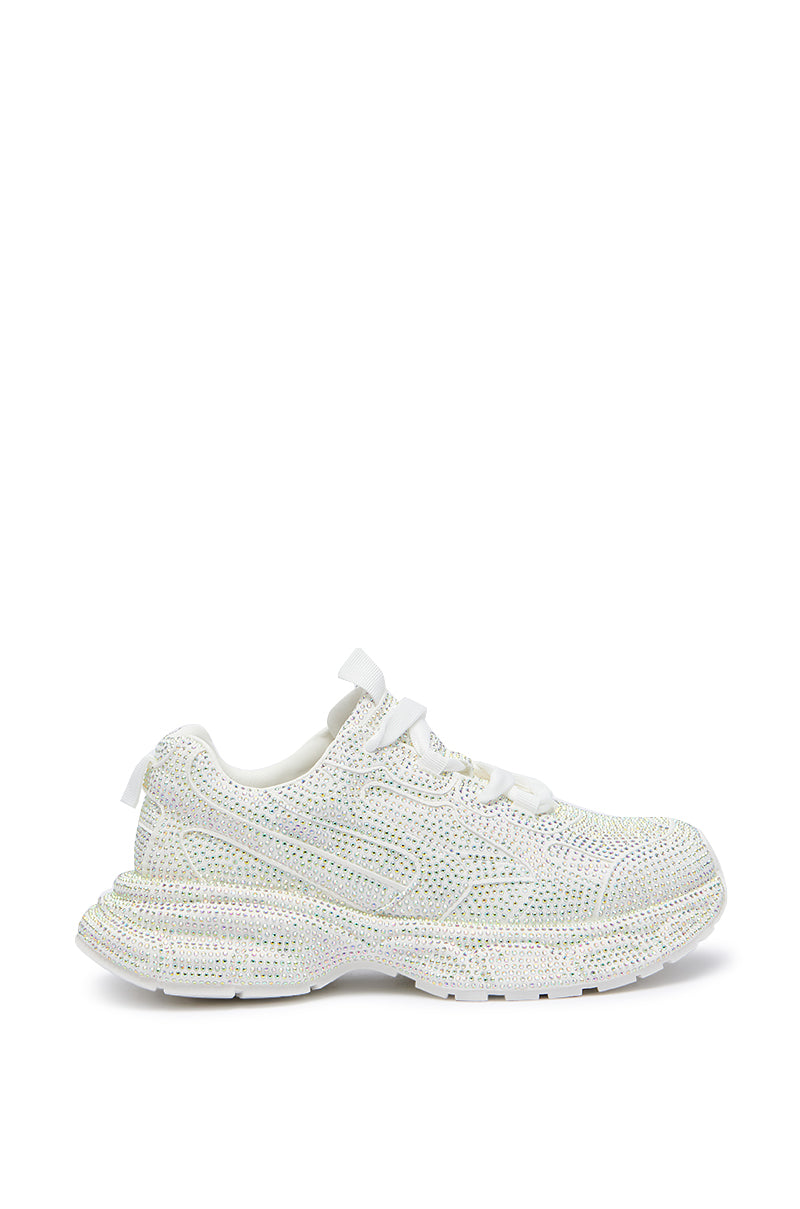 The PRINCESS WHITE EMBELLISHED SNEAKER is a stylish footwear option featuring a flatform sole and adorned with sparkling rhinestones. This trendy sneaker, often nicknamed the "princess sneaker," comes in white and includes traditional laces, making it perfect for both casual and athletic wear.