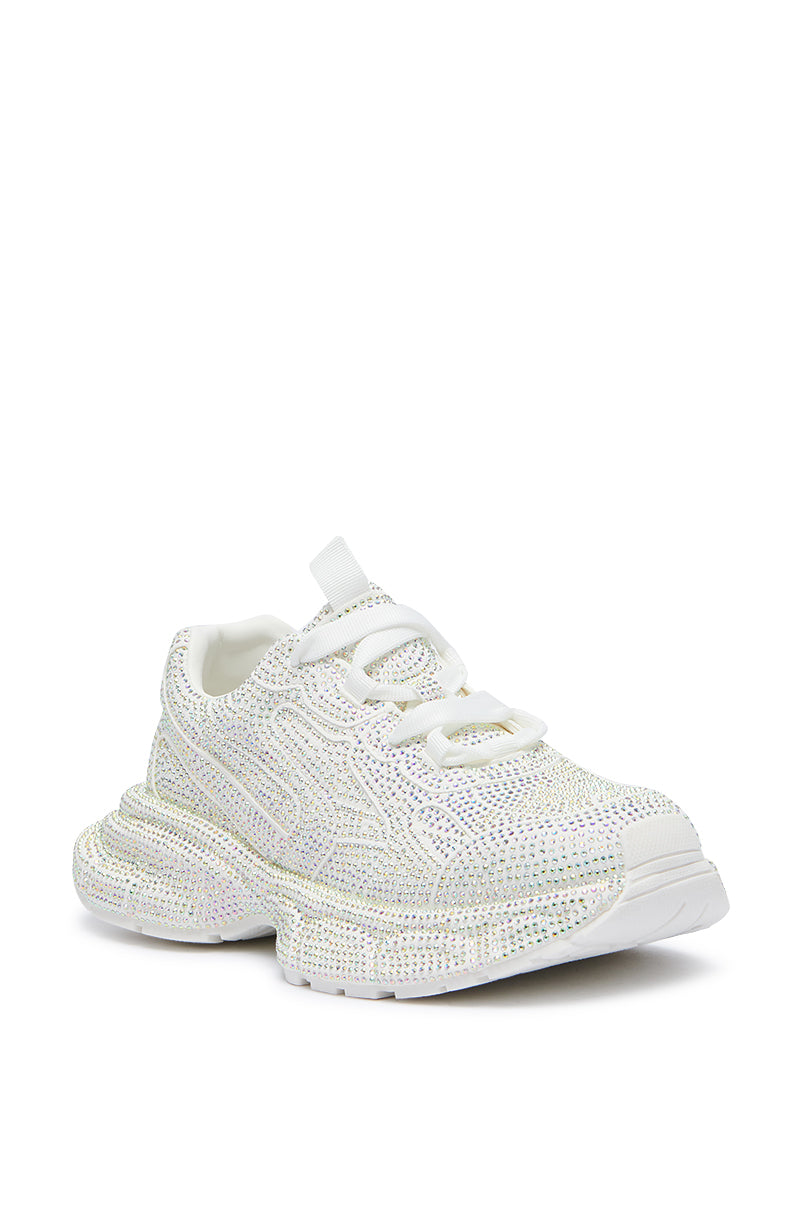 The PRINCESS WHITE EMBELLISHED SNEAKER is a white, chunky-heeled sneaker with a textured finish and rhinestone embellishments. It features a lace-up front and has a glittery or iridescent sparkle. The design includes a thick flatform sole for added height and comfort, making it the perfect princess sneaker for any wardrobe.