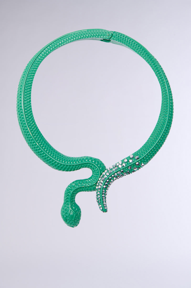 The I BITE STATEMENT NECKLACE features a striking, snake-inspired design with green scales and rhinestone embellishments. The circular shape of this exquisite piece is created by the slight overlap of the head and tail, while its intricate design is emphasized against a plain background.