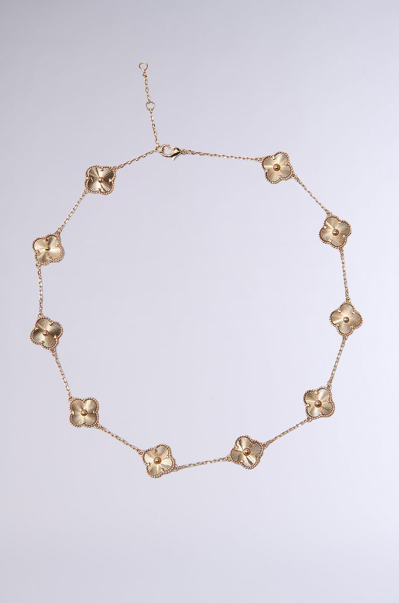 The QUEZ NECKLACE features gold-tone, textured floral charms with central beads, evenly spaced in a circular layout on a light gray background for a feminine look. 0