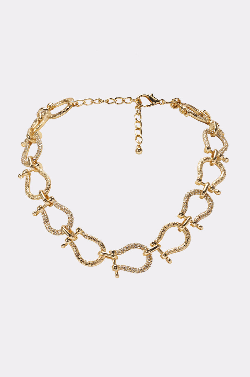 The RICH GIRL HORSEBIT NECKLACE IN GOLD features textured, wavy links adorned with signature horsebit-inspired crossbar detailing for a sophisticated touch. Finished with an adjustable clasp closure, this luxe statement piece is perfect for elevating any date night ensemble.