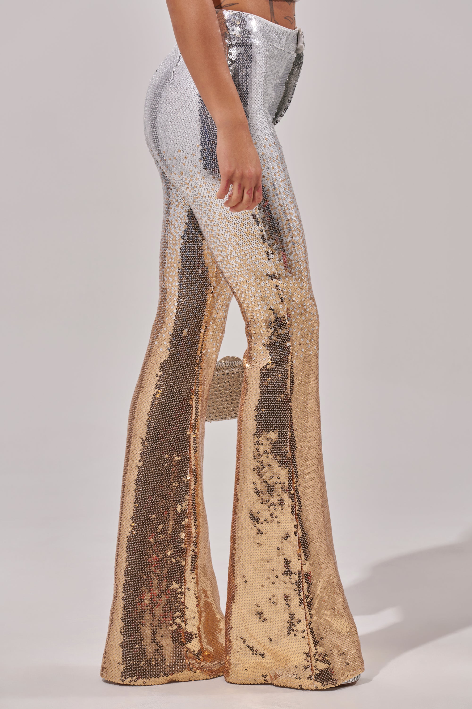 A person in the GALAXY OMBRE SEQUIN FLARE PANT—featuring silver-to-gold ombre sequins—stands against a plain light background.