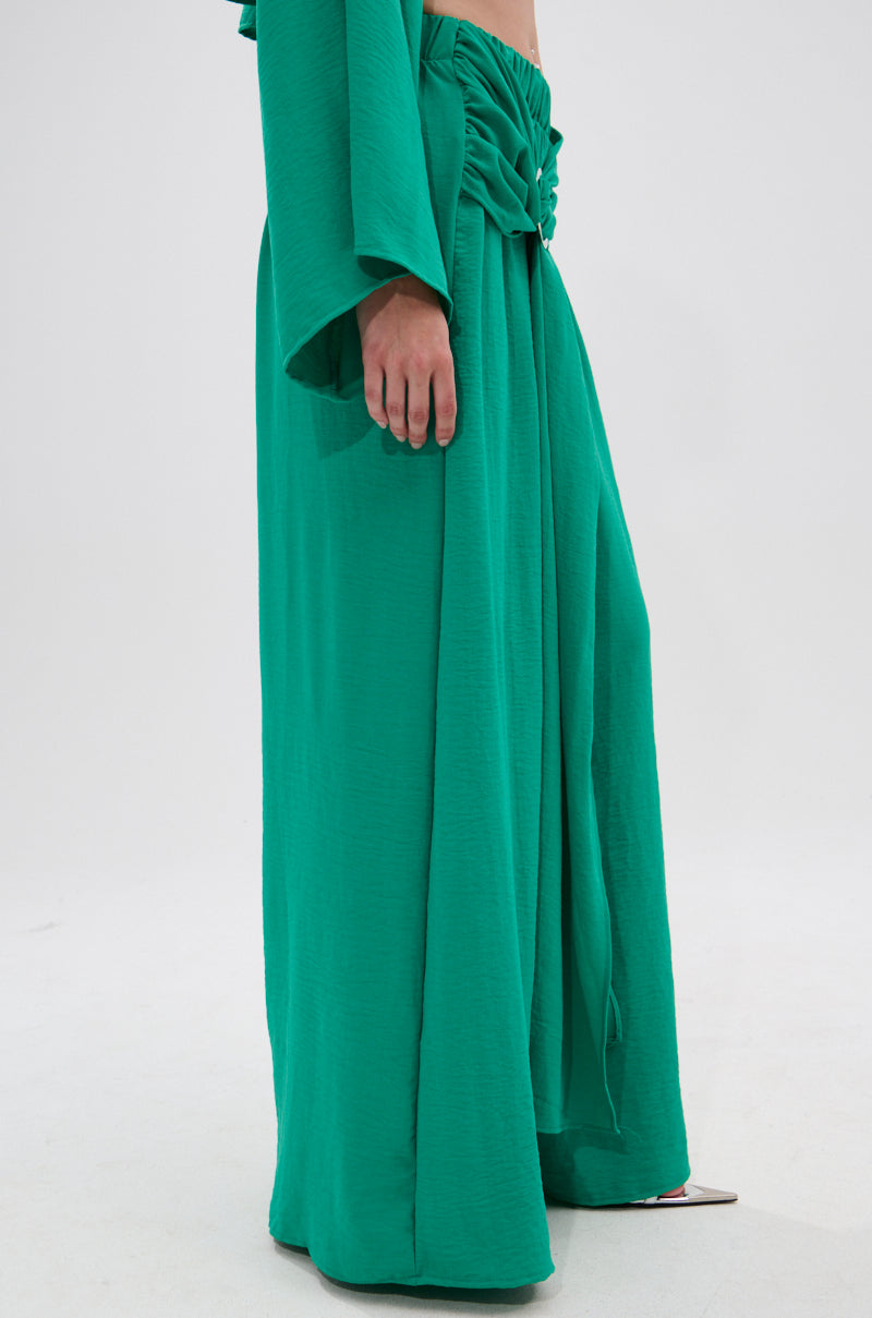 A person models the CALL ME LATER PALAZZO PANT—a bright green, wide-leg pant with a gathered, ruched waistband. Only the lower half of the outfit and part of one arm are visible against a plain white background. 2