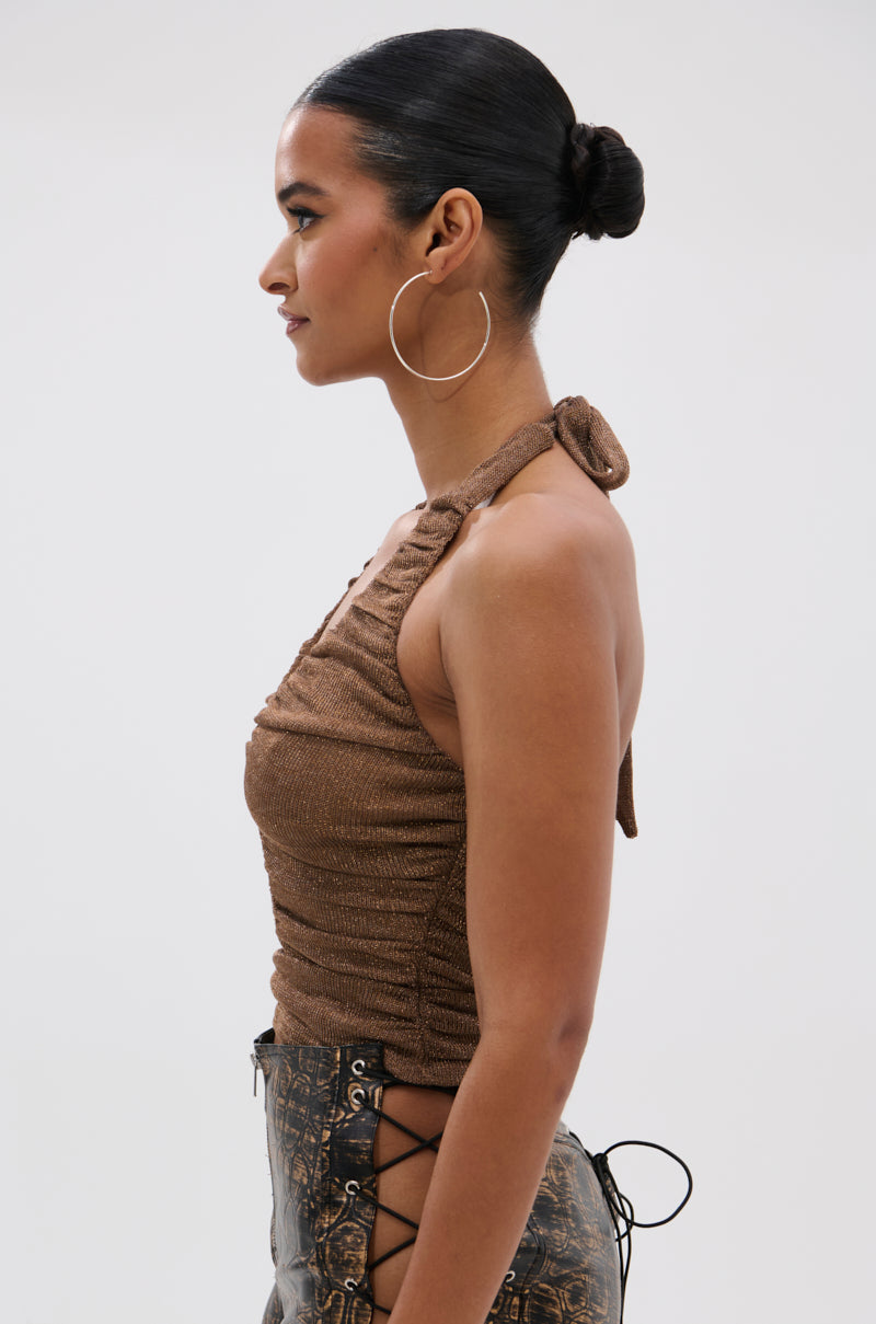 A woman in profile wears the DEEP IN LOVE SLINKY HALTER NECK top with large hoop earrings and side lace-up pants; her dark hair is styled in a sleek bun, set against a plain light background.