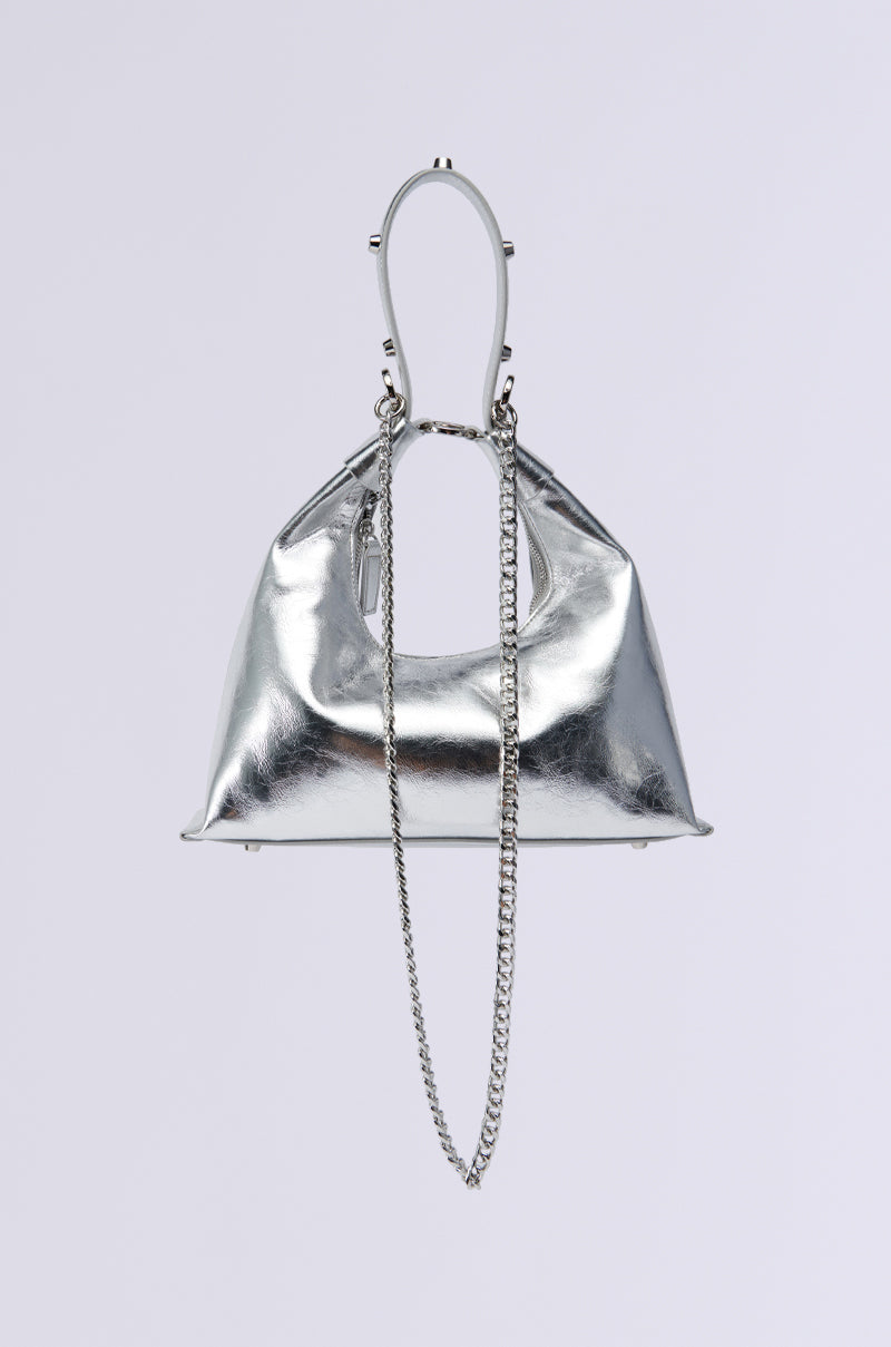 The TOO TRENDY PURSE is a chic accessory featuring a faux silver metallic finish, a unique curved handle, and a long chain strap. Its elegant design shines brightly, appearing as if suspended against a plain white background.