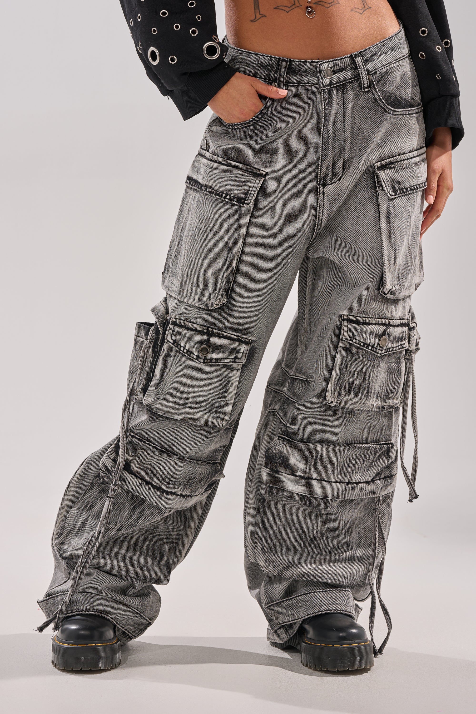 Someone wearing the CARGO FOR DAYS CARGO DENIM PANT—loose, wide-leg denim cargo jeans with multiple large pockets and ties—paired with chunky black shoes. Only the lower body is shown against a plain background. 1