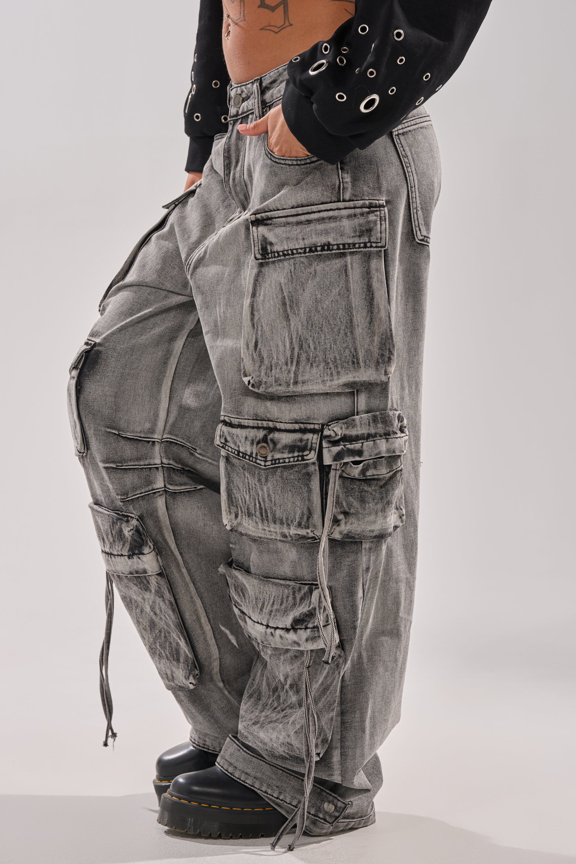 Wearing the CARGO FOR DAYS CARGO DENIM PANT in acid-washed gray with wide legs, large pockets, and drawstrings, styled with black platform shoes and a black long-sleeve grommet-detail shirt. 2