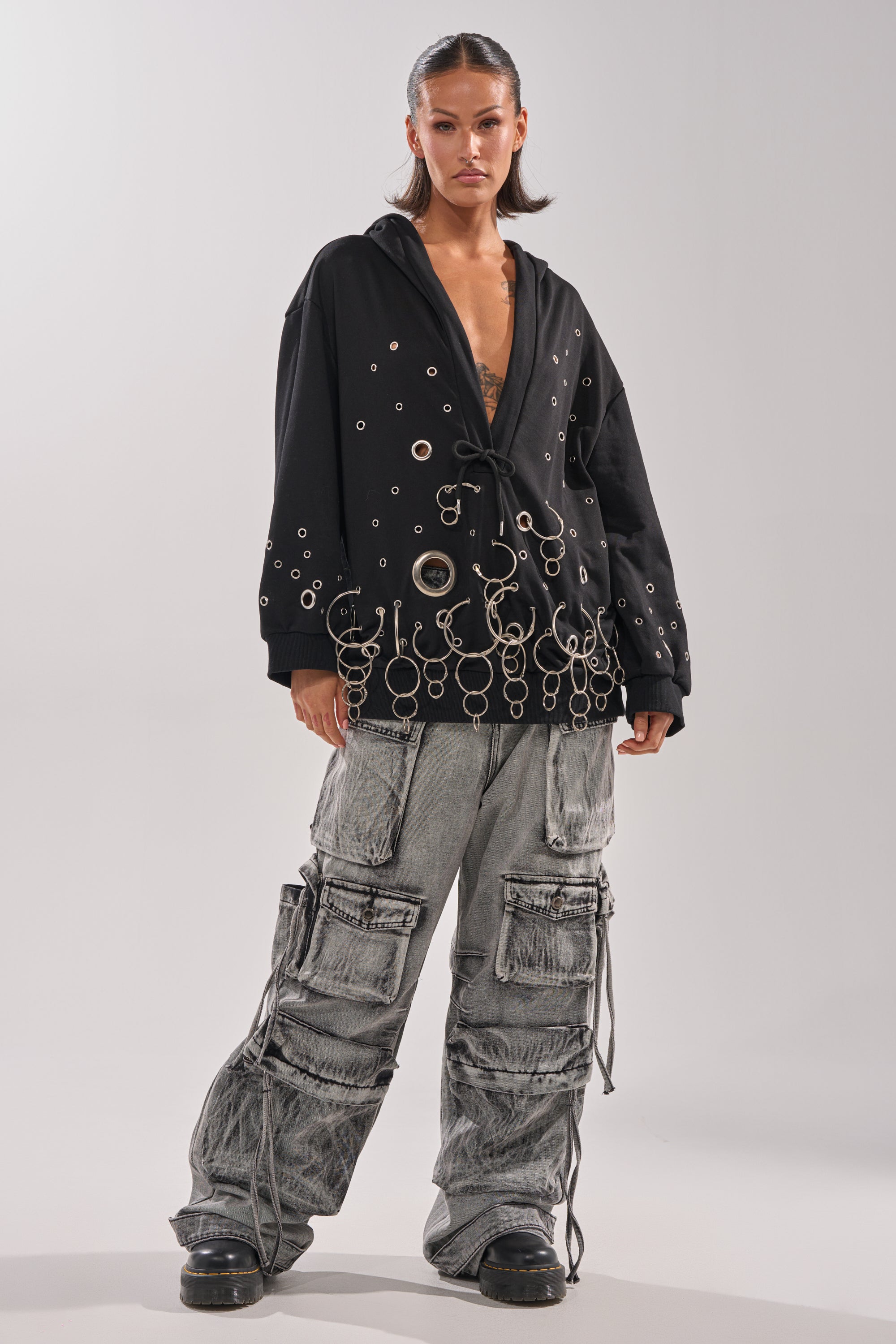 A woman stands confidently in an oversized black hoodie and chunky shoes, paired with the CARGO FOR DAYS CARGO DENIM PANT featuring drawstrings and multiple pockets. 4