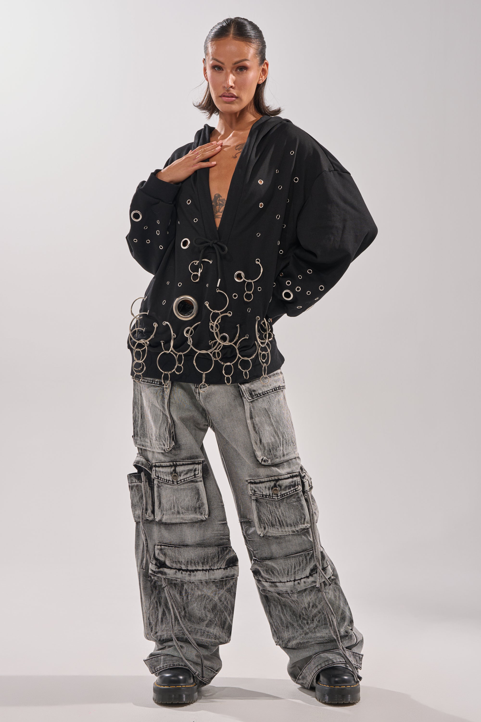 A person stands confidently in a black oversized top with metal eyelets and rings, paired with the CARGO FOR DAYS CARGO DENIM PANT—loose, wide-leg denim pants with multiple large pockets—and chunky black shoes. 5