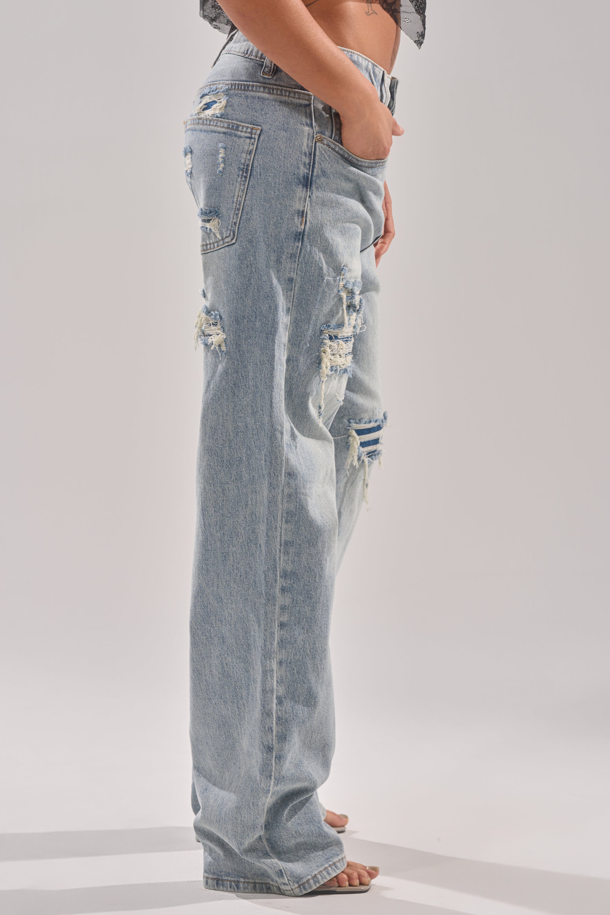 A person stands barefoot in side profile, left hand in pocket, wearing RUN AWAY WITH ME RELAXED DENIM high-rise jeans against a plain light background. 3